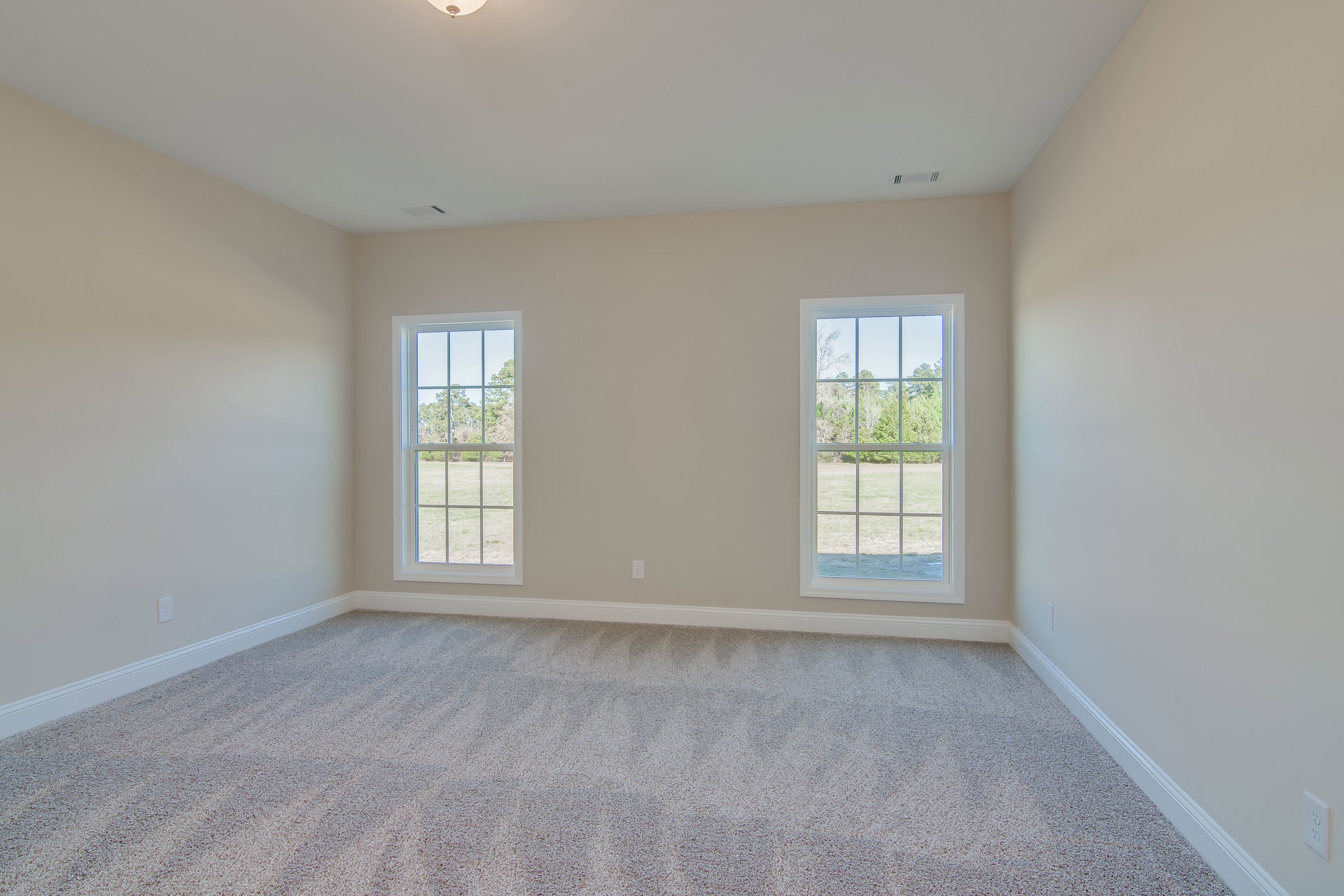 Carpeted room with white walls, large windows showing trees and grass outside, white ceiling with recessed light fixture