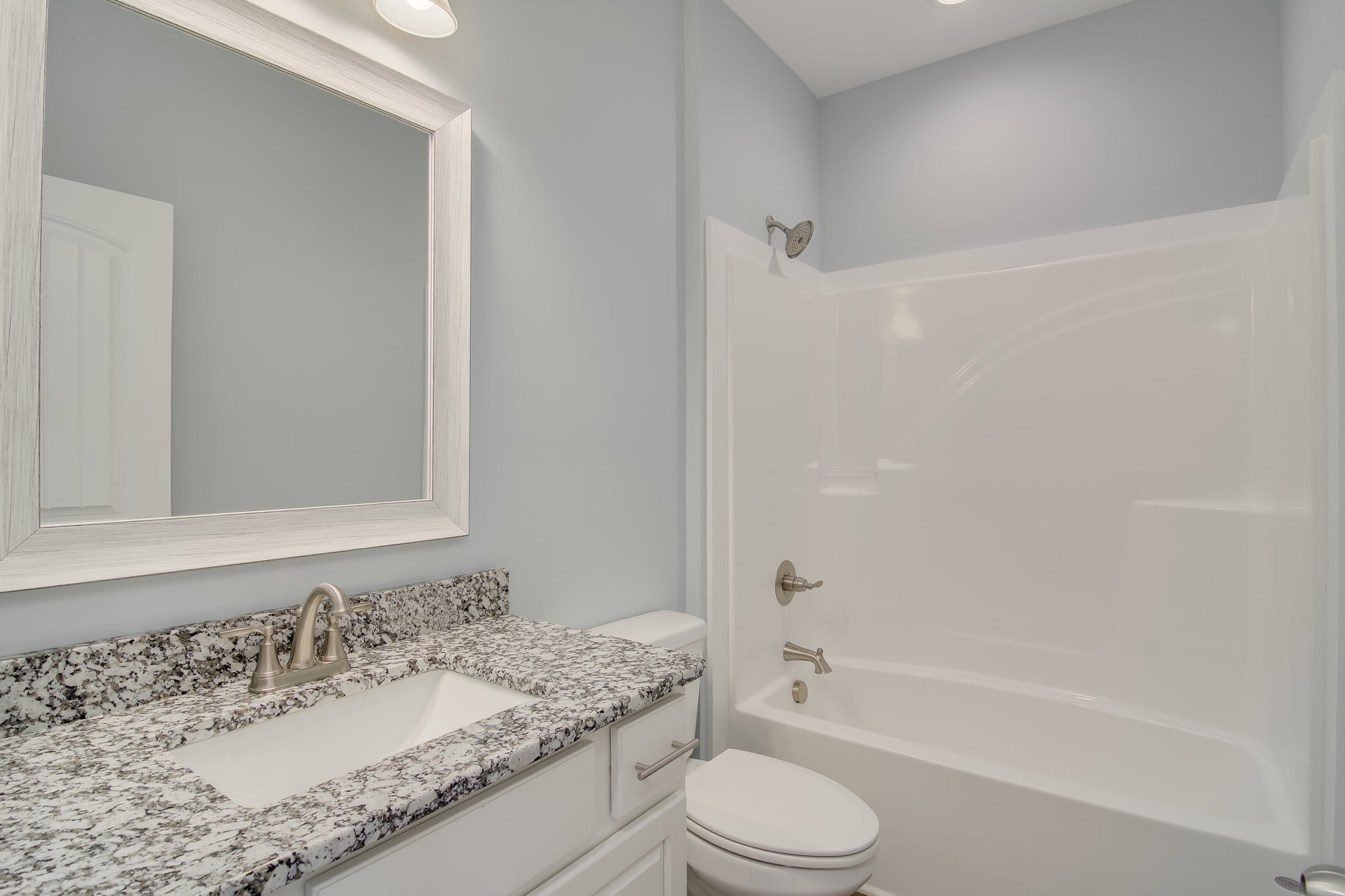 Bathroom with white tile walls, built-in bathtub, white toilet with lid up, rectangular sink with chrome faucet, large wall-mounted mirror above vanity