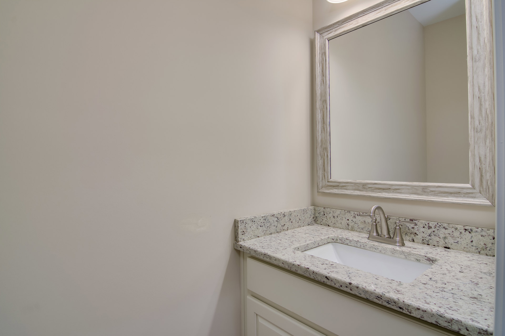 White bathroom with rectangular wall mirror above a stone countertop, chrome faucet, undermount sink, and light gray tile backsplash