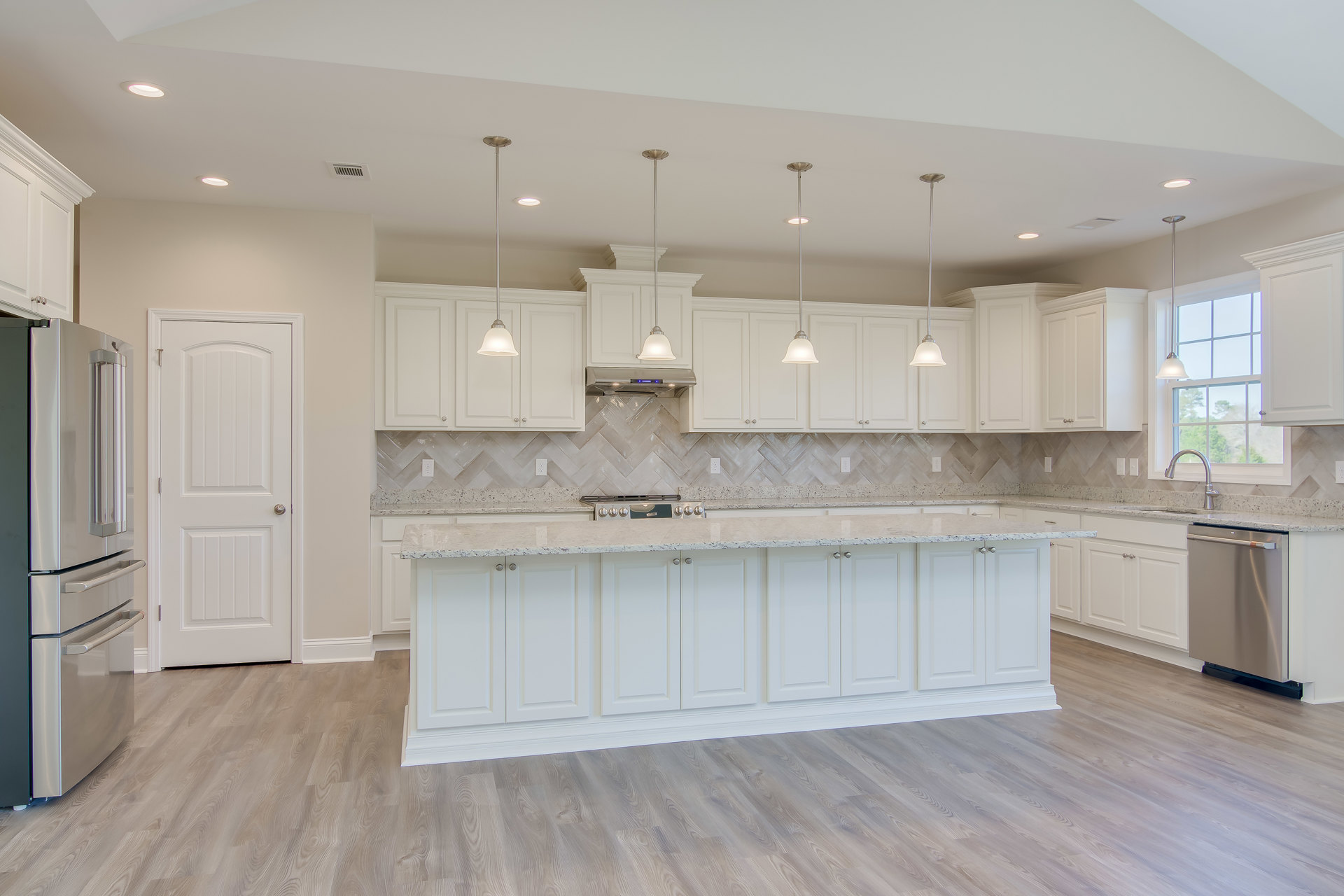 White kitchen with marble countertops, stainless steel refrigerator, white cabinetry island, silver door knob on white door, tiled floor, and white ceiling