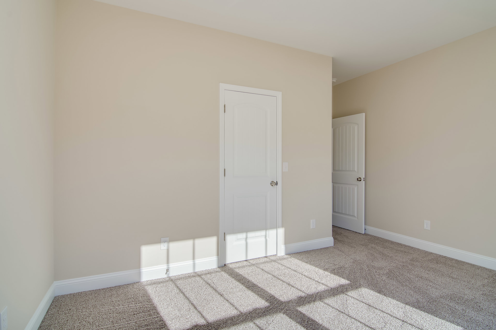White door with silver knob set in a white wall, beige carpeted floor, soft natural light casting shadows across the room.