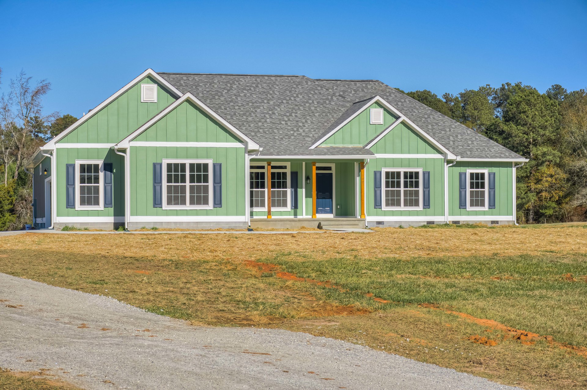 Green house with white porch, blue front door, white-trimmed windows, manicured lawn, and paved driveway