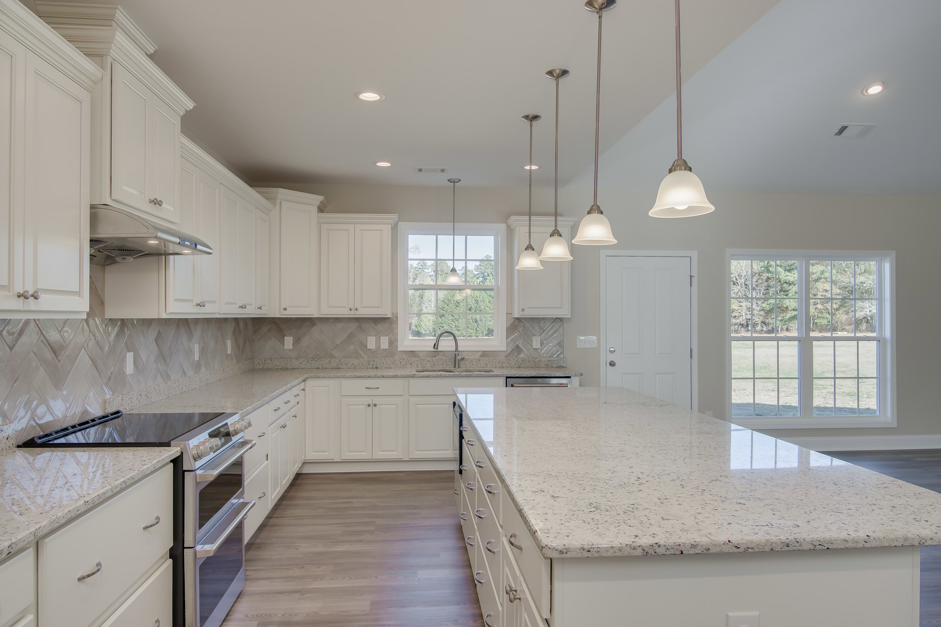 White kitchen cabinets with granite countertops, stainless steel sink beneath a window overlooking trees, pendant light fixture, and modern appliances.