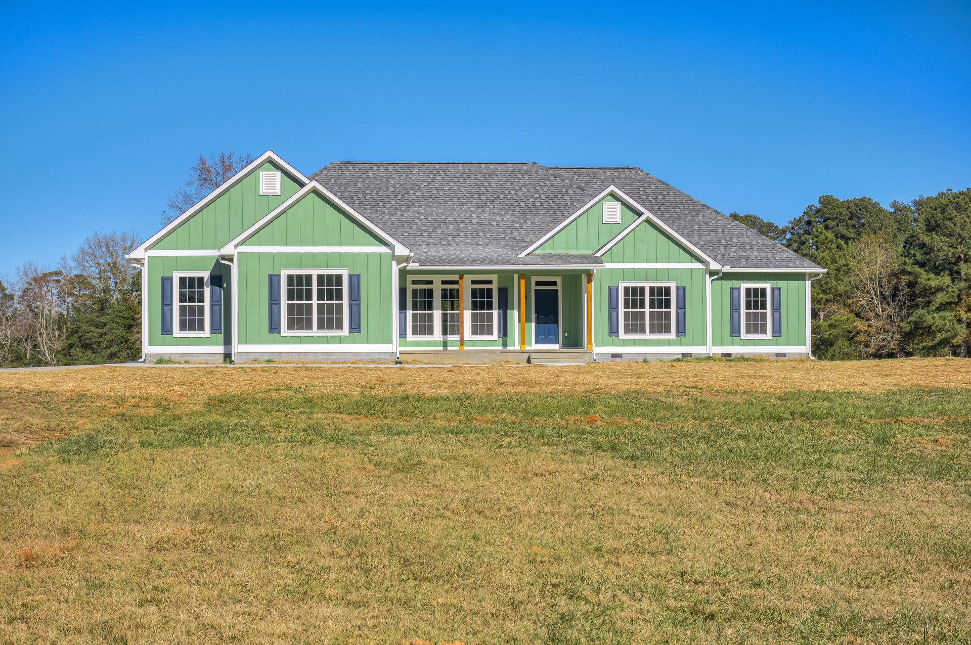 Green-painted house with white-framed windows, blue and white doors, green roof, and manicured lawn surrounded by trees and plants.