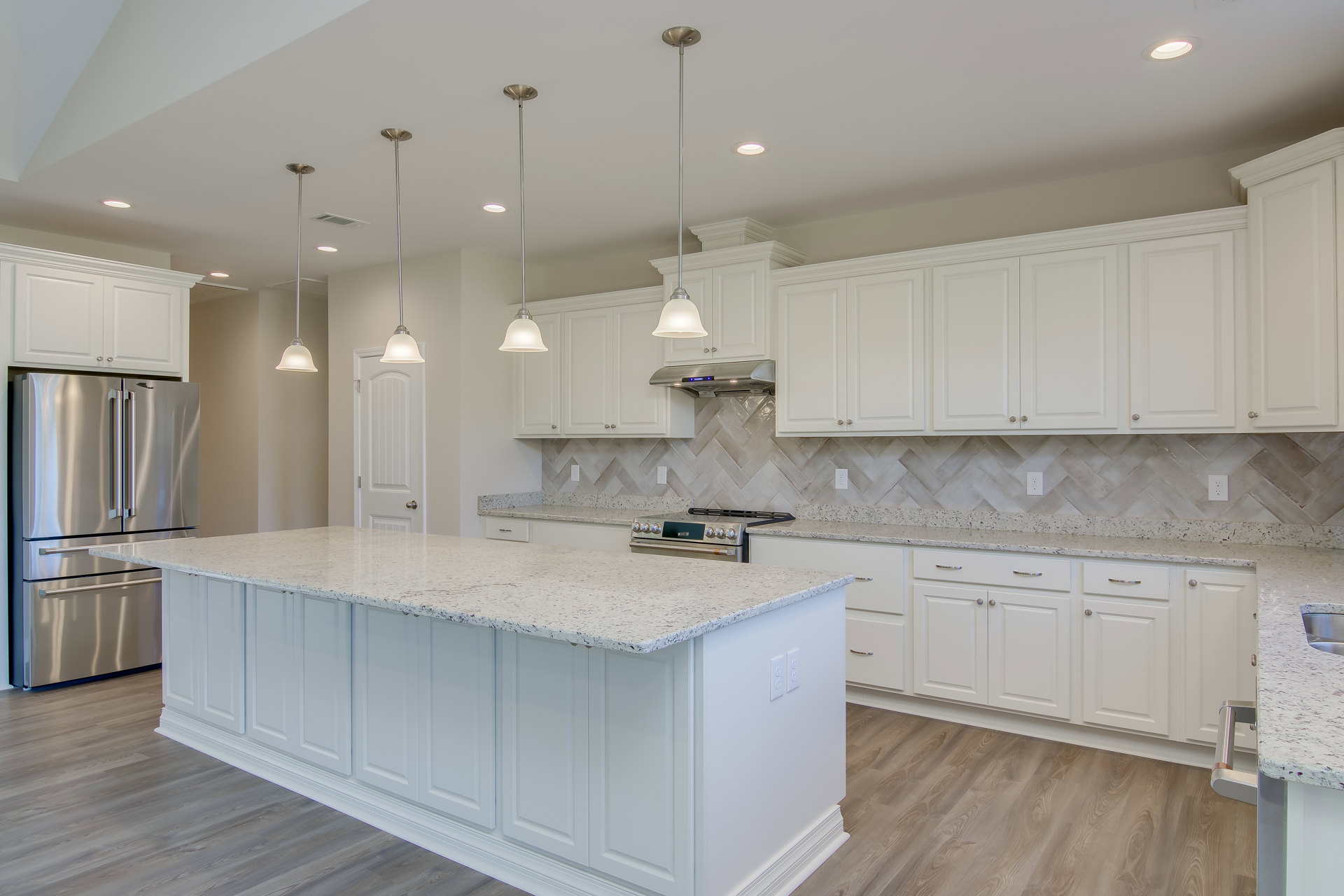 White kitchen cabinets, marble countertops, stainless steel refrigerator, tile backsplash, undermount sink, pendant light fixture, granite island, light wood flooring