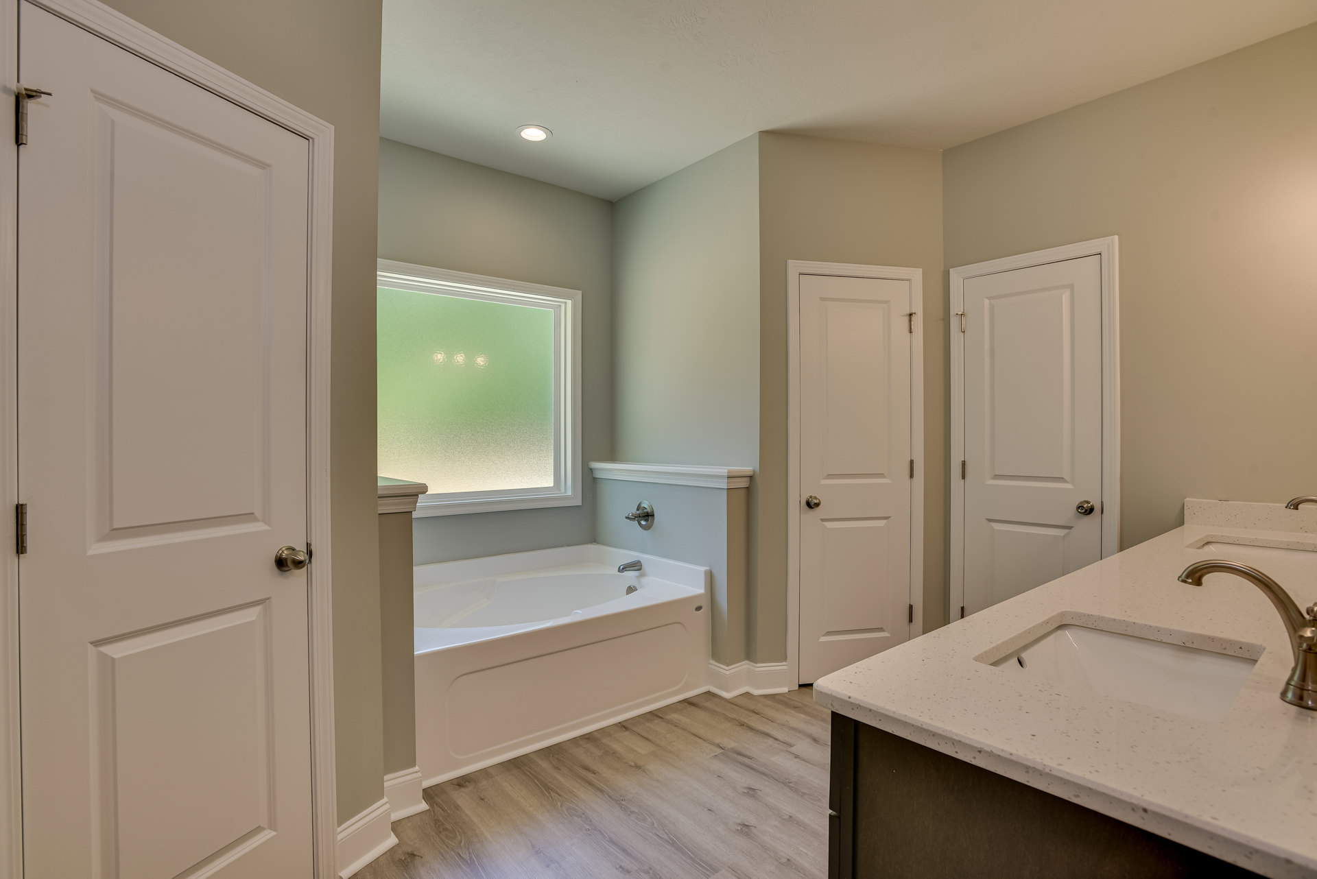 Bathroom with freestanding bathtub, rectangular sink on wood vanity, large mirror, frosted glass window, white door with silver doorknob, light tile flooring and walls