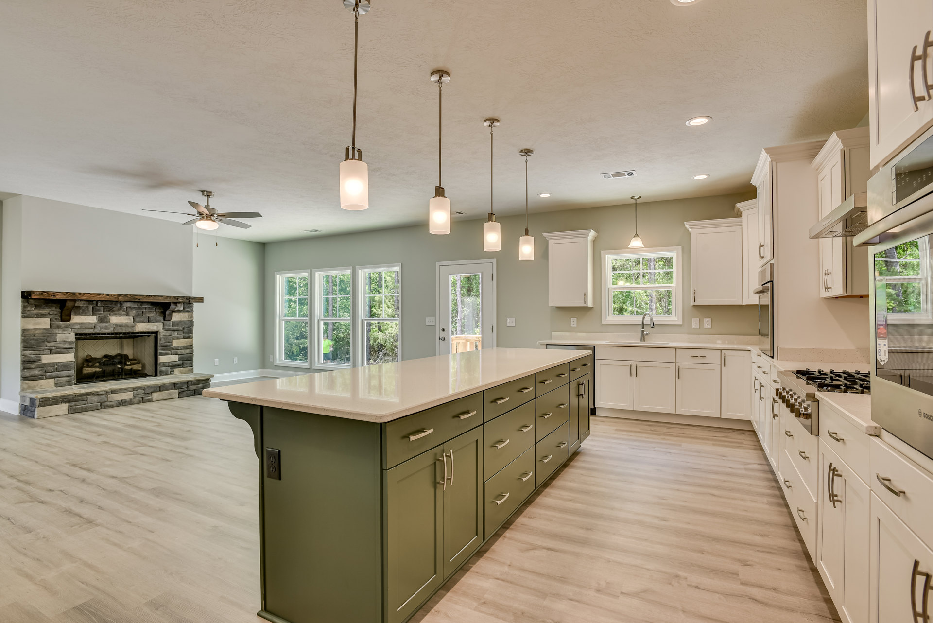 Spacious kitchen featuring a large island with drawers and cabinets, stone fireplace with wood log, metal bar stools, pendant lights above white countertop, window over sink
