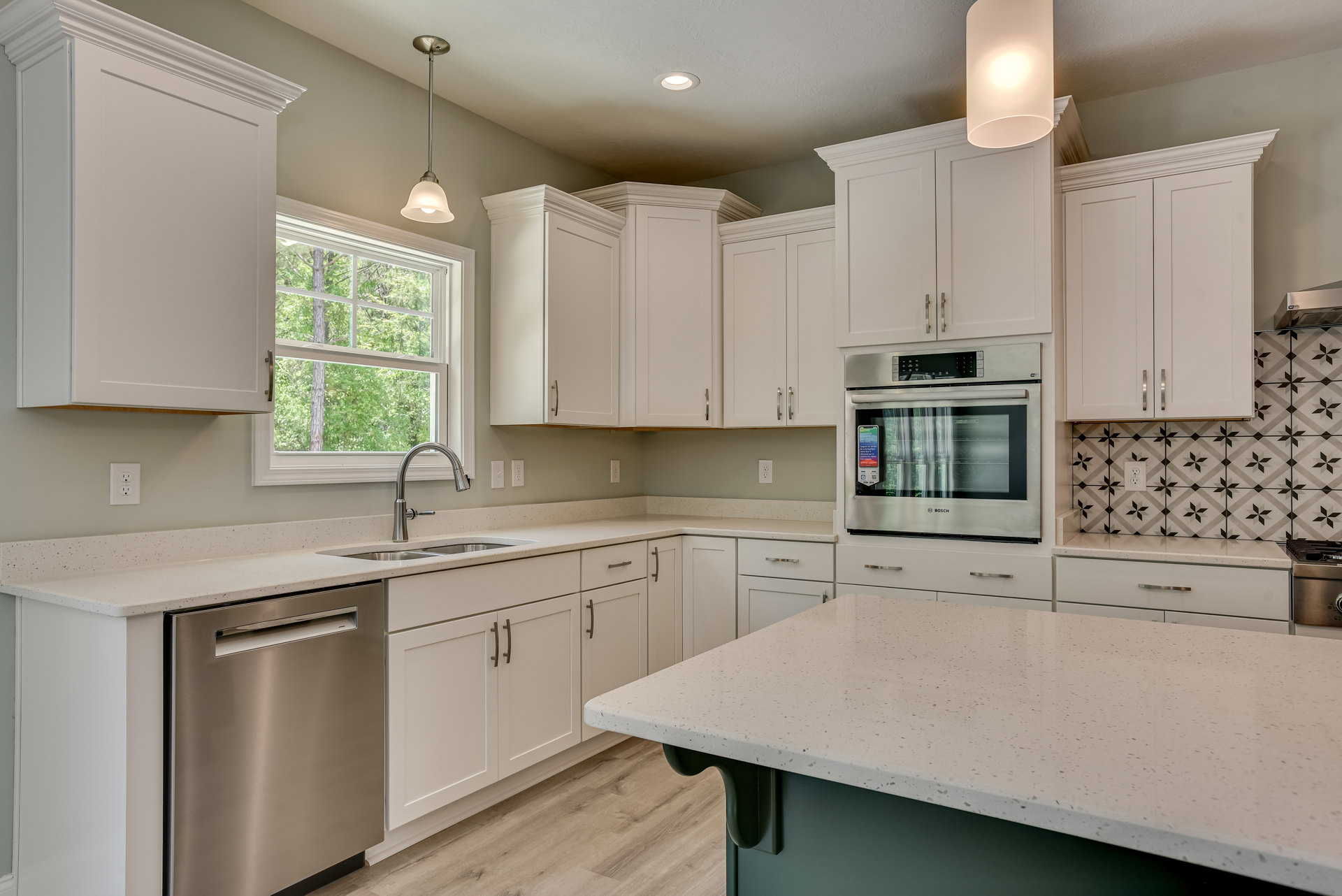 White kitchen with shaker cabinets, speckled quartz countertop, stainless steel oven, silver refrigerator, under-cabinet lighting, and reflective backsplash.