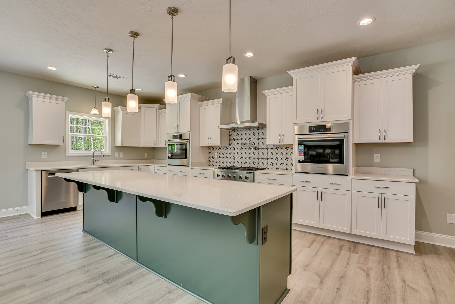 White kitchen with shaker cabinets, large central island featuring a white countertop, built-in microwave on the wall, stainless steel fixtures, and recessed lighting illuminating