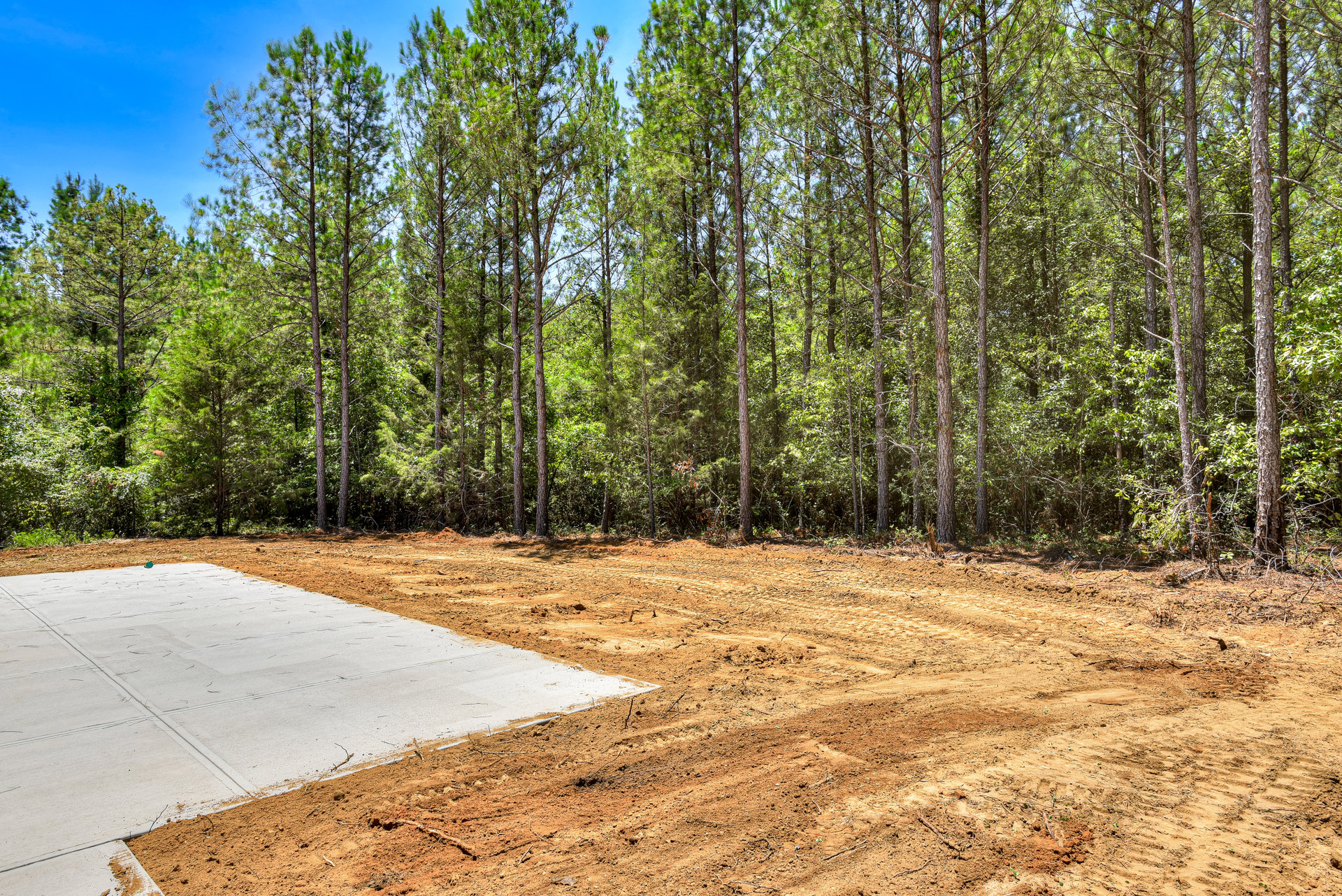 Concrete slab set in a dirt field bordered by tall trees, dirt road with tire tracks leading through natural landscape
