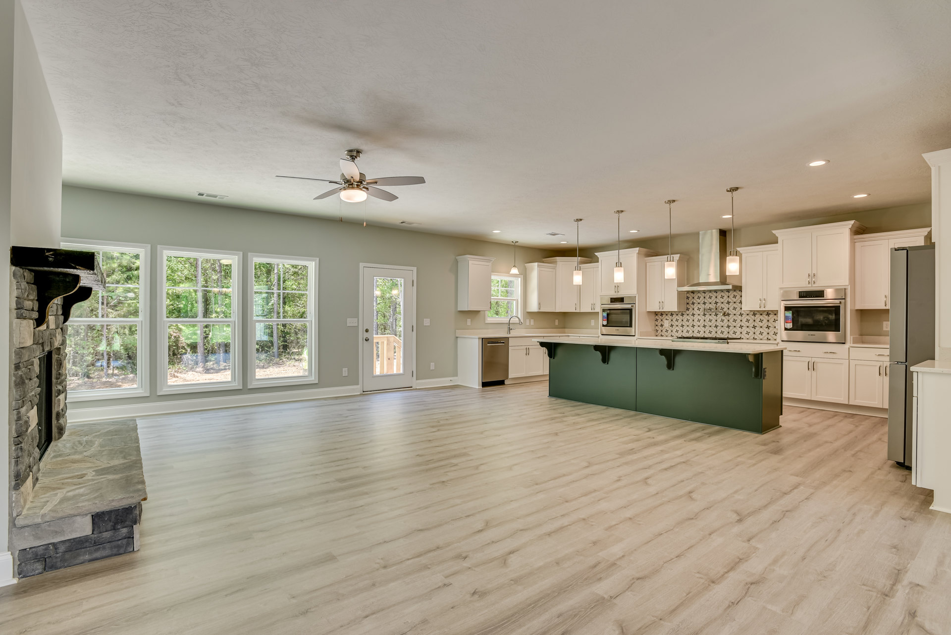 Spacious open-concept living area featuring a central kitchen island with white countertops, wood flooring, ceiling fan, modern cabinetry, stainless steel appliances, fireplace
