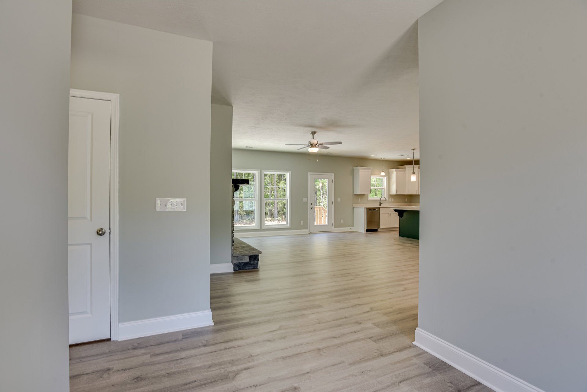 Wood flooring in a bright room with a ceiling fan, glass-paneled door, stone accent wall, and window overlooking trees.