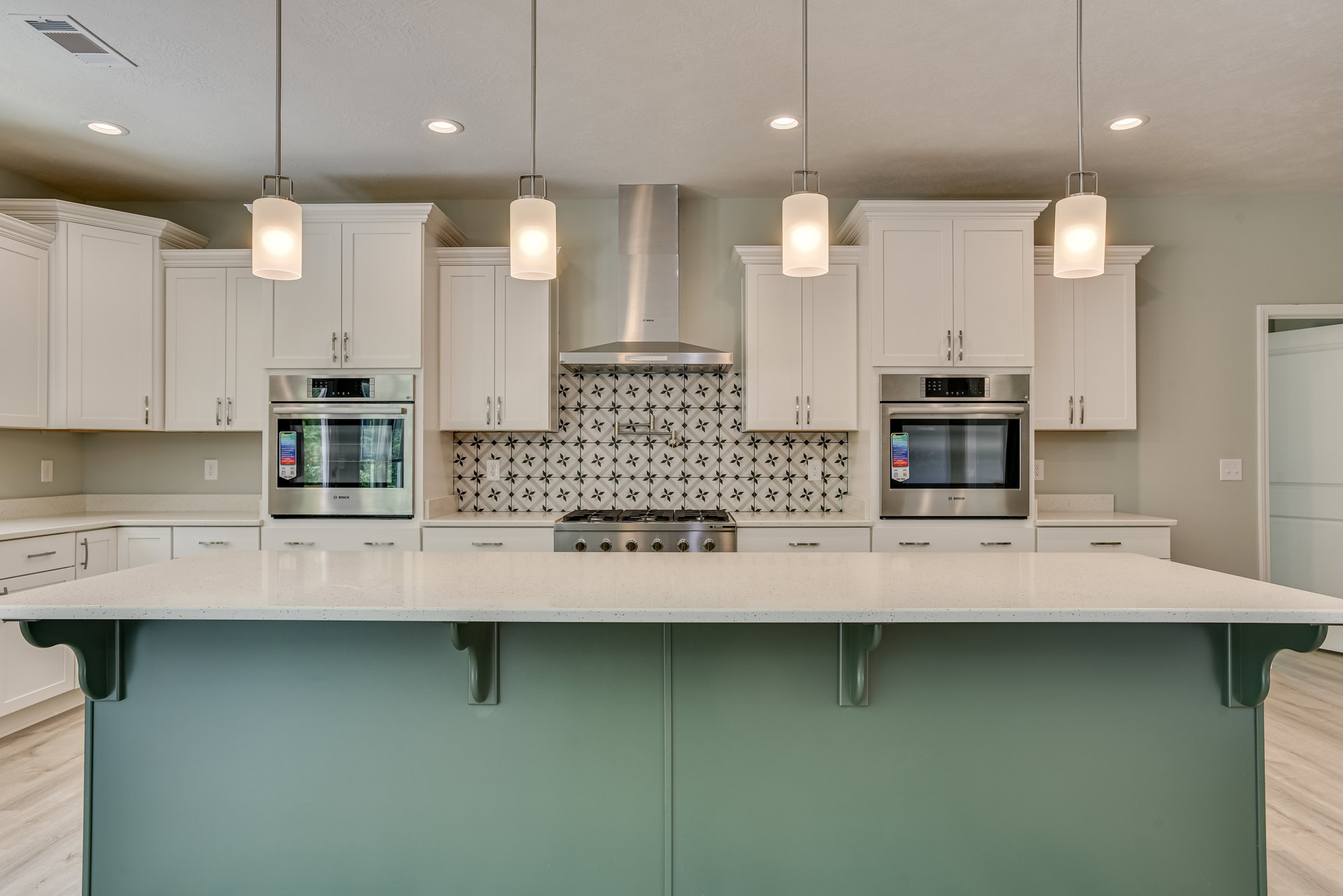Kitchen with white shaker cabinets, green island with quartz countertop, stainless steel oven with digital display, farmhouse sink, pendant lighting, and hardwood flooring