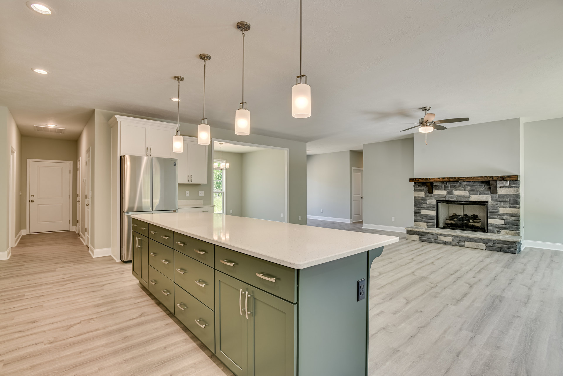 Spacious kitchen featuring a large island with drawers and cabinets, stainless steel refrigerator, white cabinetry, wood flooring, built-in fireplace with stacked logs, modern