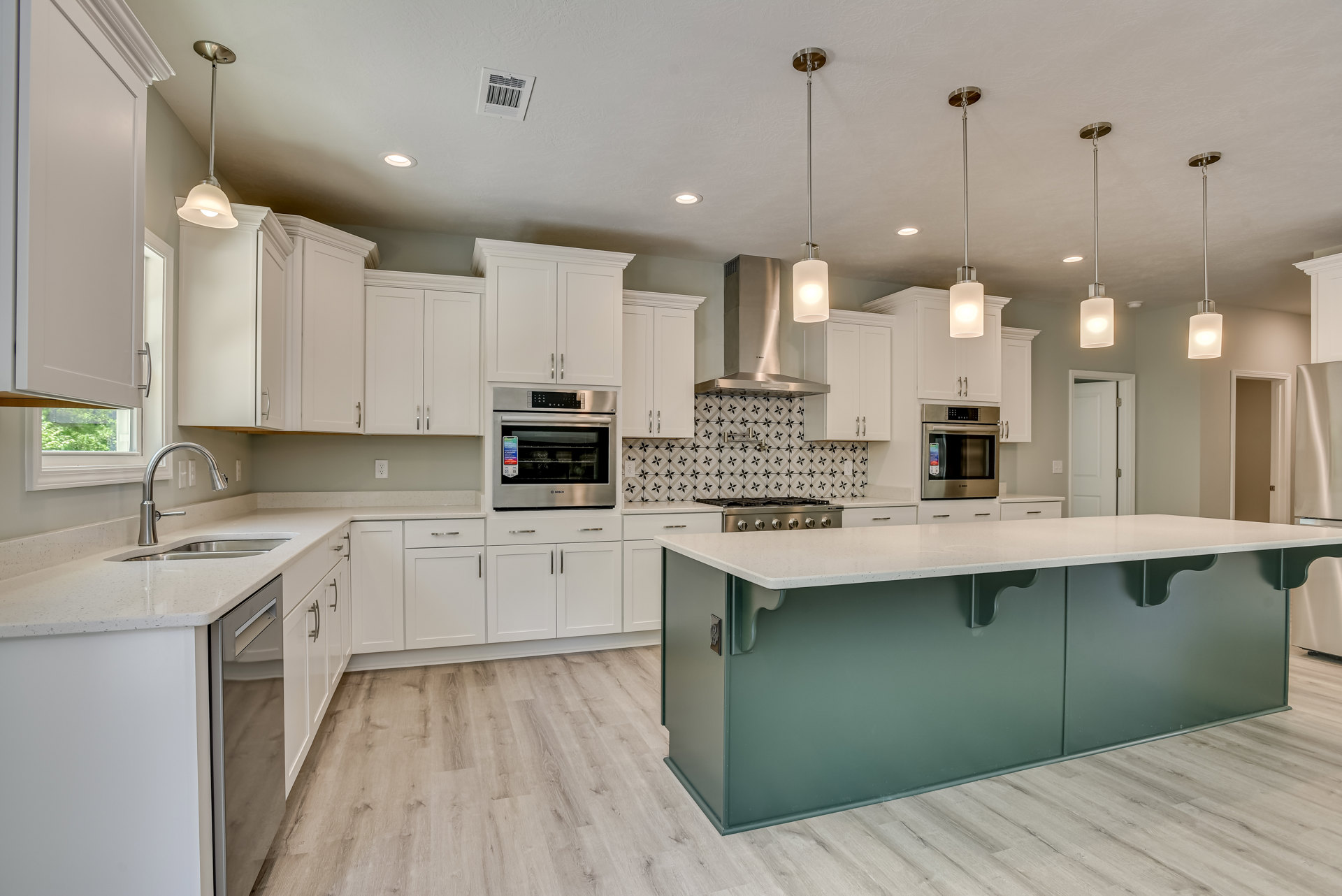 White kitchen with shaker cabinets, central island featuring quartz countertop, stainless steel oven and microwave, undermount sink, and recessed lighting above light hardwood