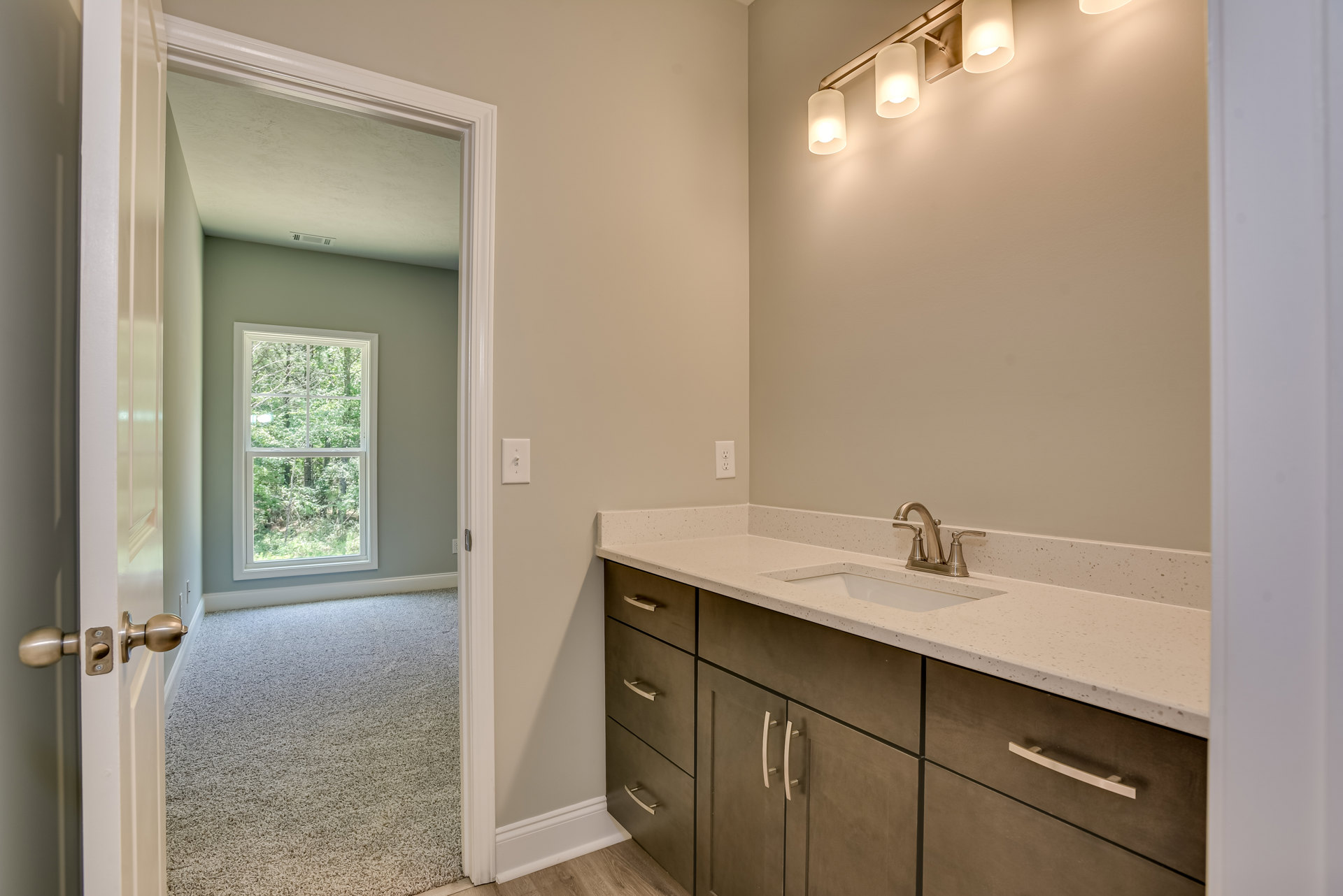 Bathroom with white tile walls, wood vanity cabinet, chrome faucet, white sink, frosted glass window showing trees outside, modern light fixture with white shade, and paneled door
