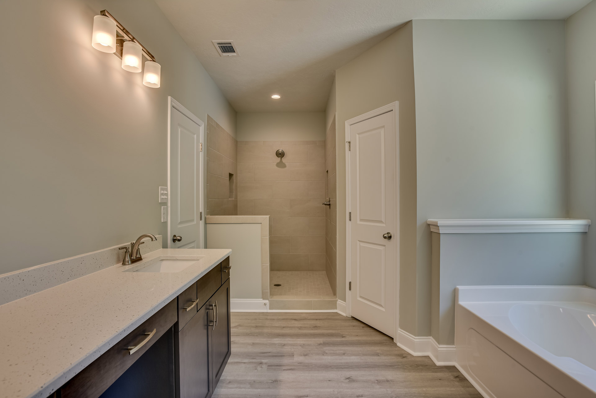 Modern bathroom featuring a glass-enclosed shower, white vanity with sink, light gray tile walls, and chrome fixtures