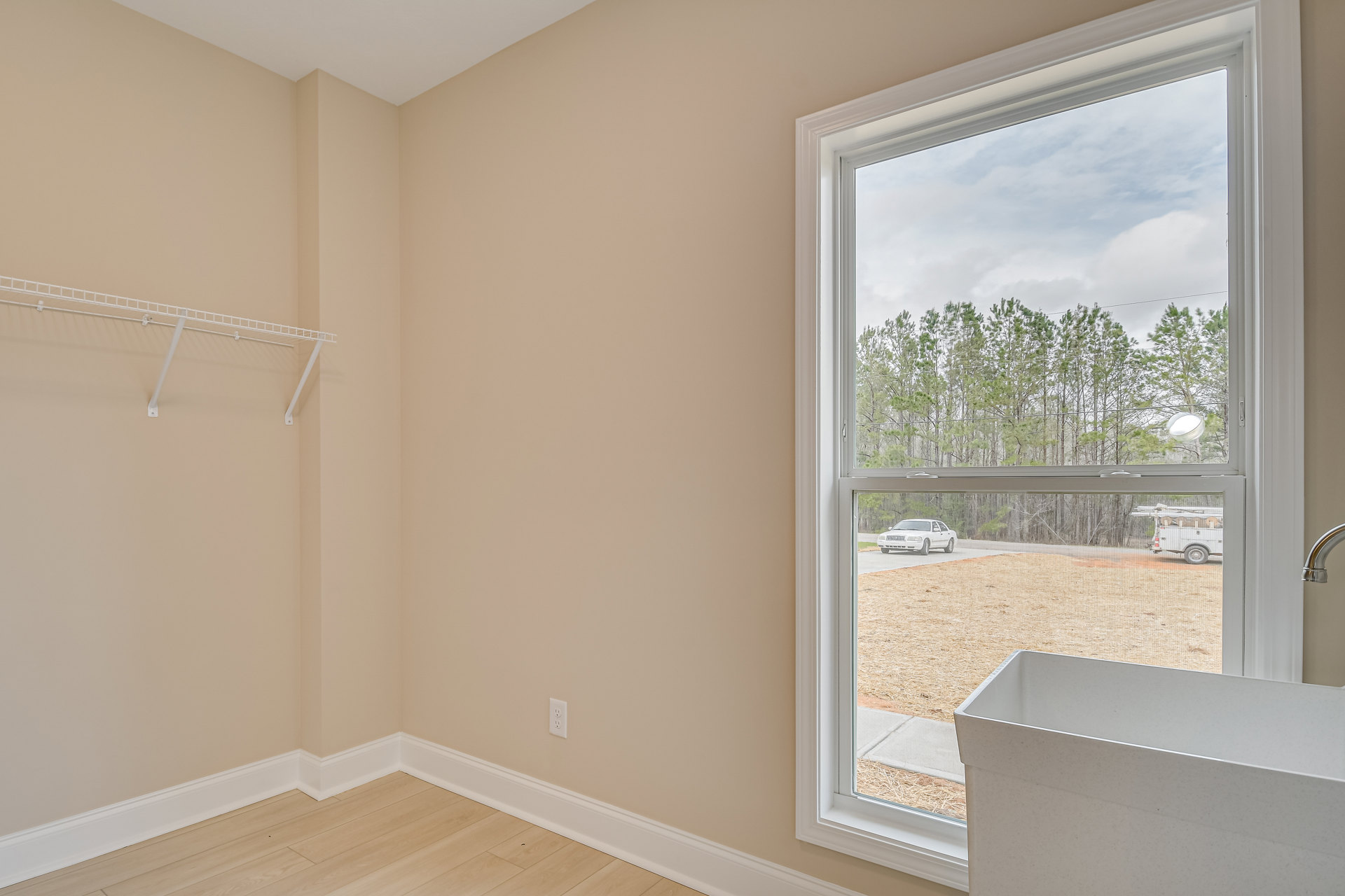 Laundry room with light-colored walls, window overlooking trees and parked car, white laundry basket on tiled floor, ceiling molding and plaster finishes visible