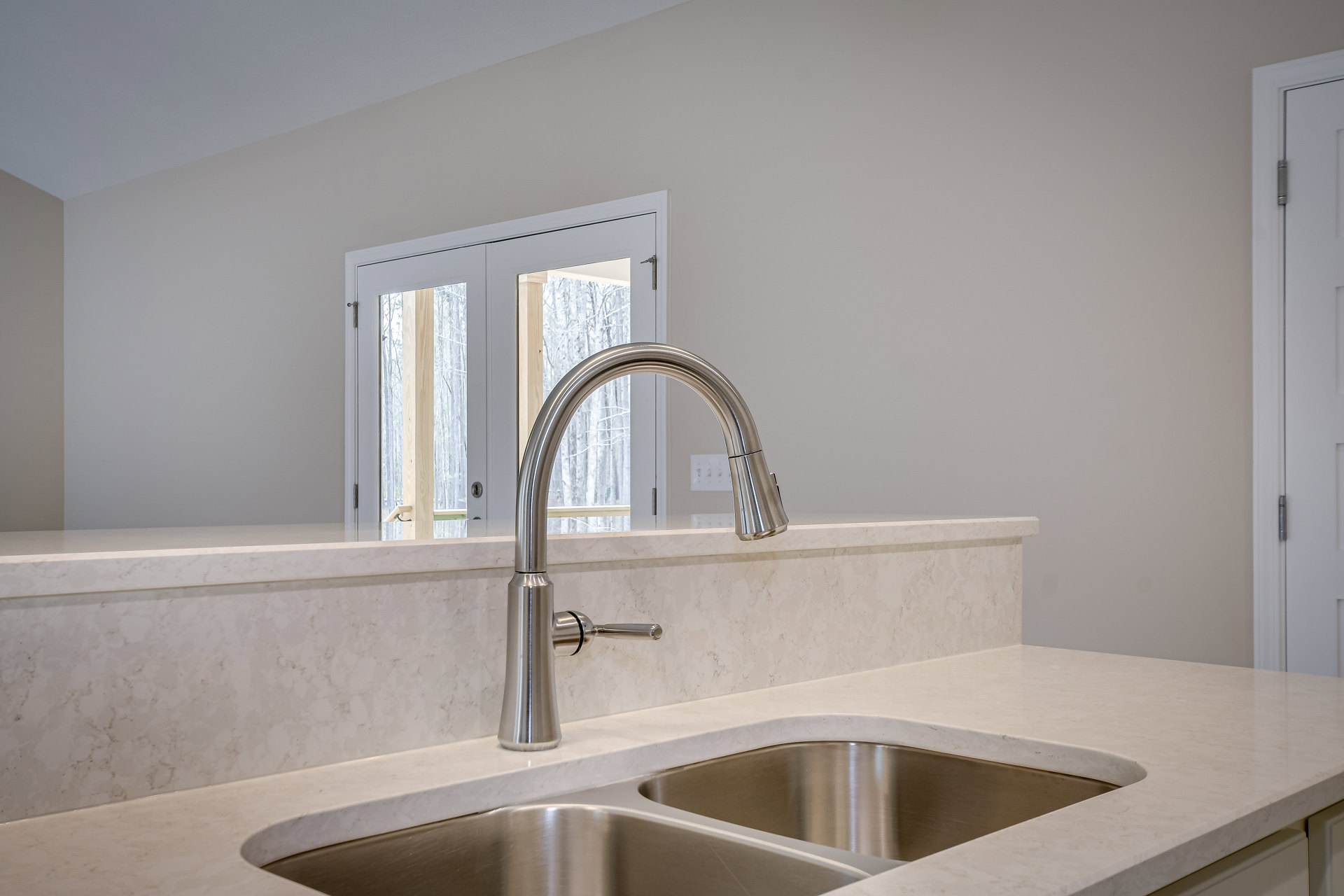 Stainless steel sink with chrome faucet set in a marble countertop, glass-paneled door and white tile backsplash in modern kitchen