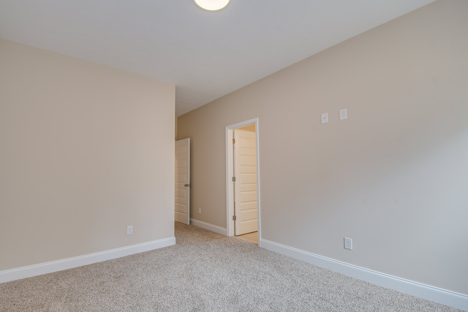 Carpeted room with white paneled door, open doorway, light fixture on ceiling, and plaster walls with crown molding