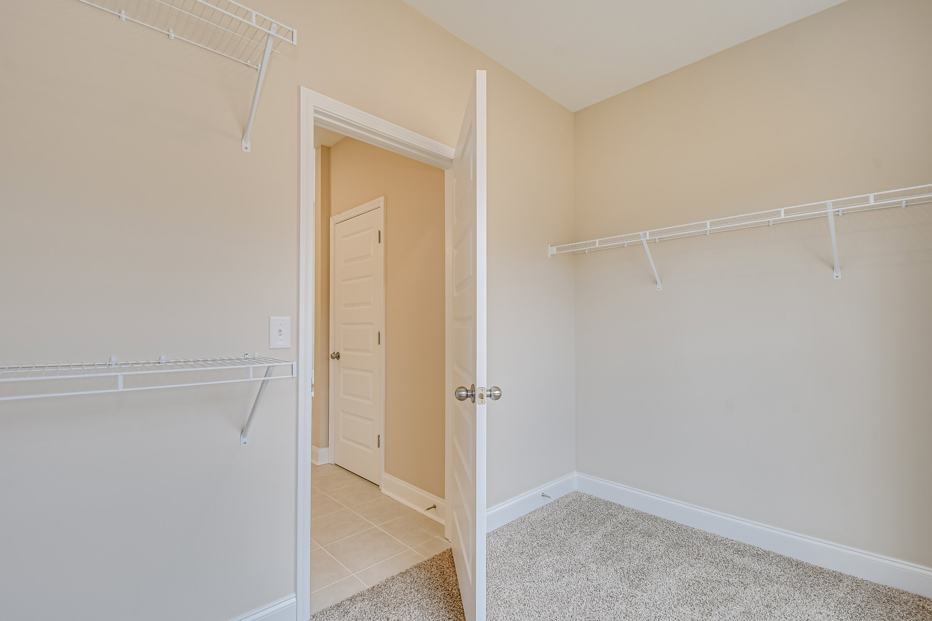 White closet with open door, built-in shelves, white tile flooring, and a patterned rug