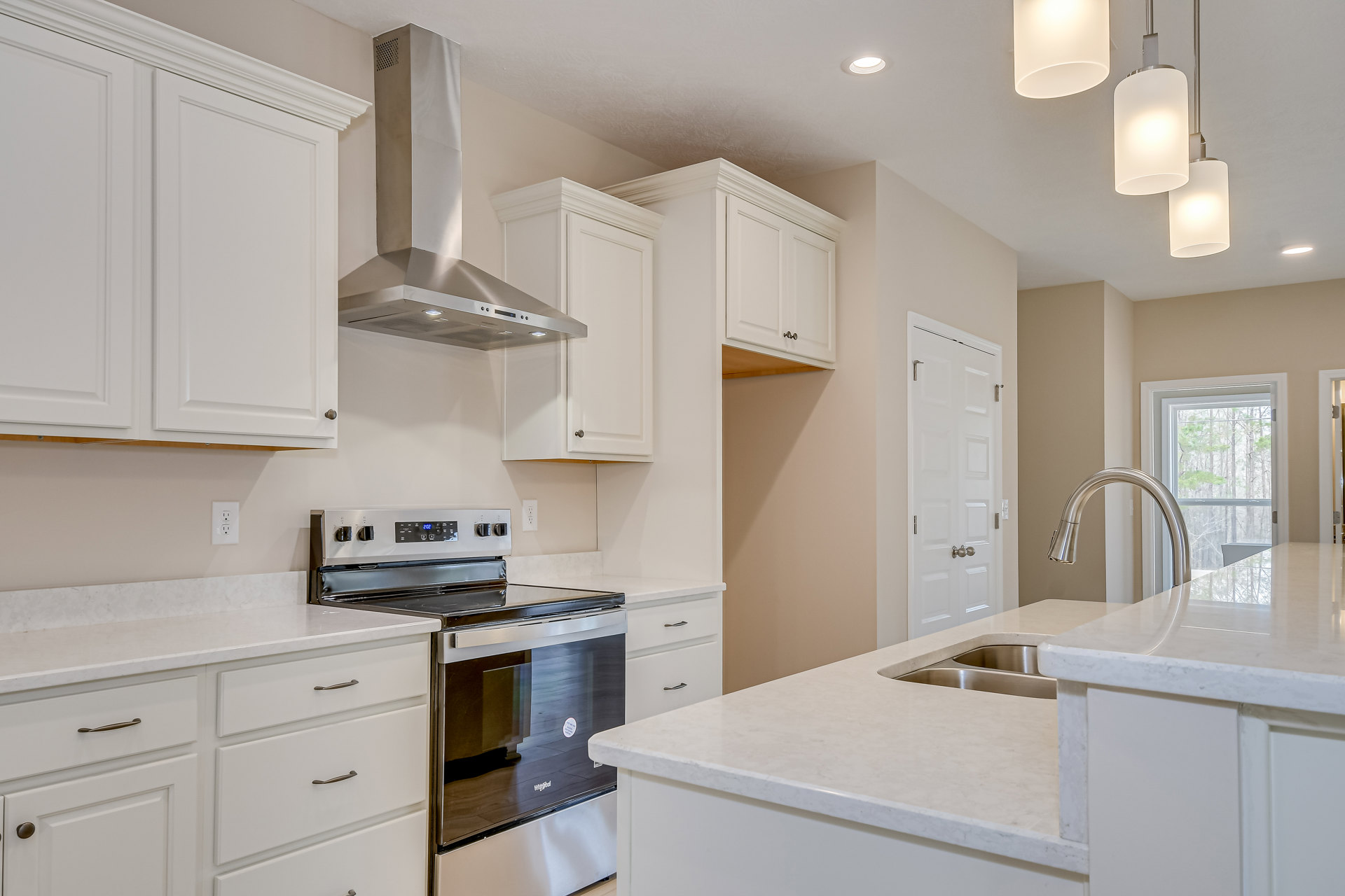 White shaker cabinets, stainless steel stove and oven, quartz countertops, silver hardware, window overlooking trees, glass door, pendant lamp above kitchen island