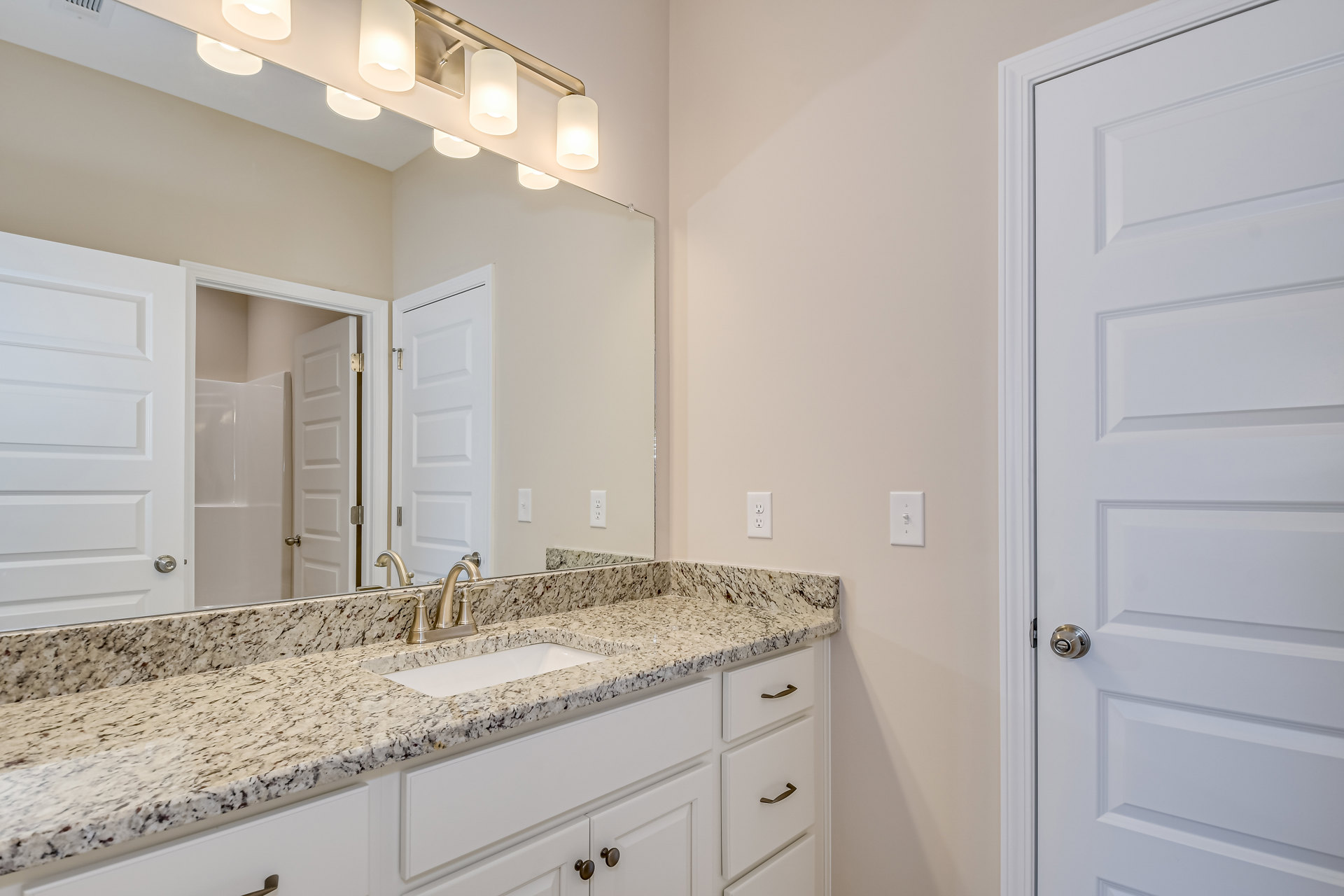 Marble bathroom countertop with undermount sink, chrome faucet, large framed mirror, white cabinetry, and wall-mounted light fixture