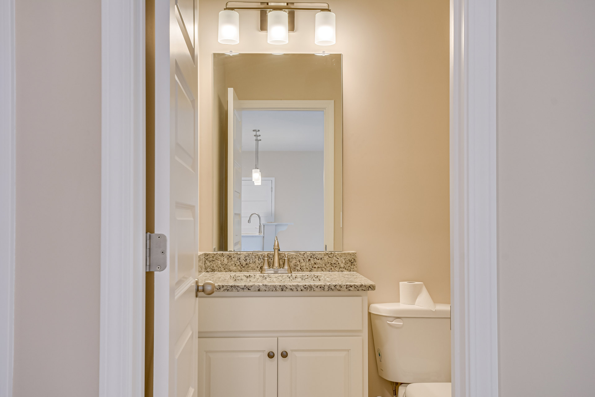 Bathroom with white tile walls, pedestal sink with chrome faucet, wall-mounted mirror, toilet with toilet paper on tank, illuminated white light fixture, and light streaming in