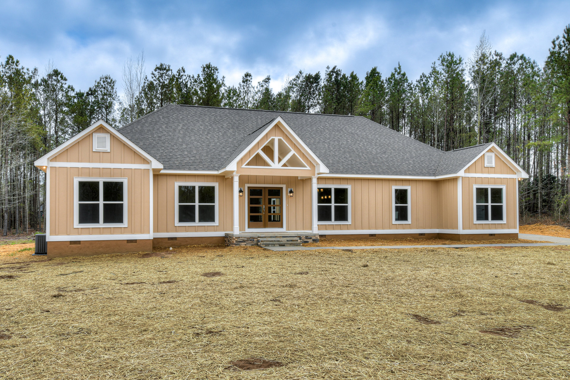 Two-story custom home with white siding, double glass entry doors, white-framed windows, covered porch with steps, expansive green lawn, and mature trees under a partly cloudy sky.