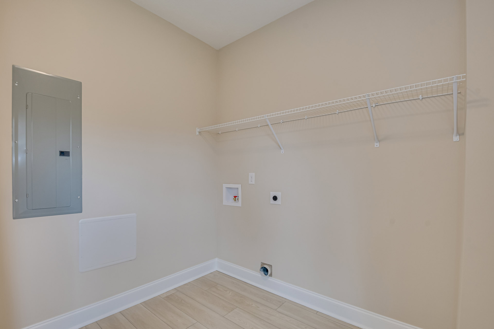 Bathroom with white plaster walls, built-in white shelf, wood flooring, and a white framed box with two valves mounted beside a white door