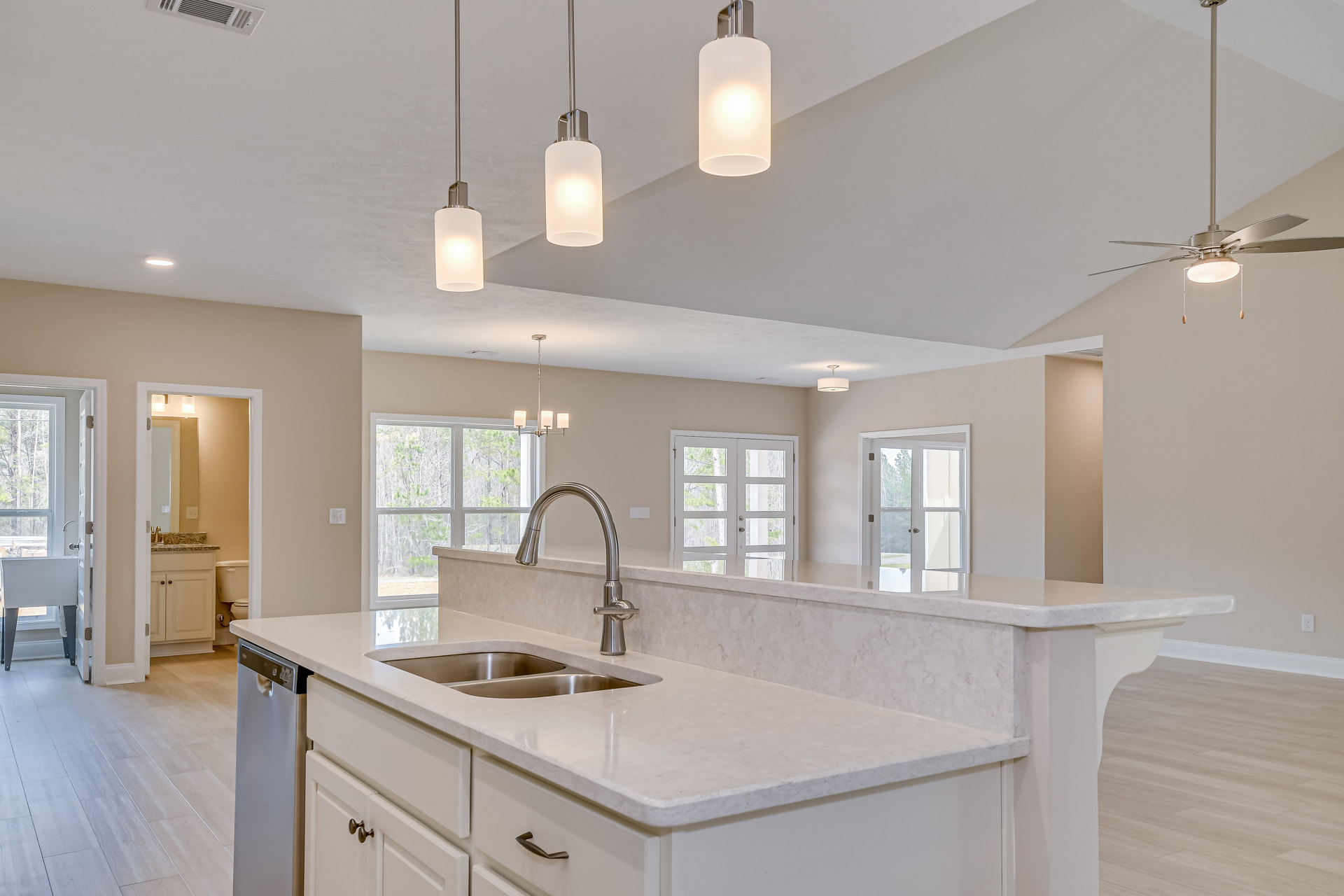 Modern kitchen featuring two stainless steel sinks set in a stone countertop, white cabinetry, tile backsplash, double glass-paneled doors, and a ceiling light illuminating a