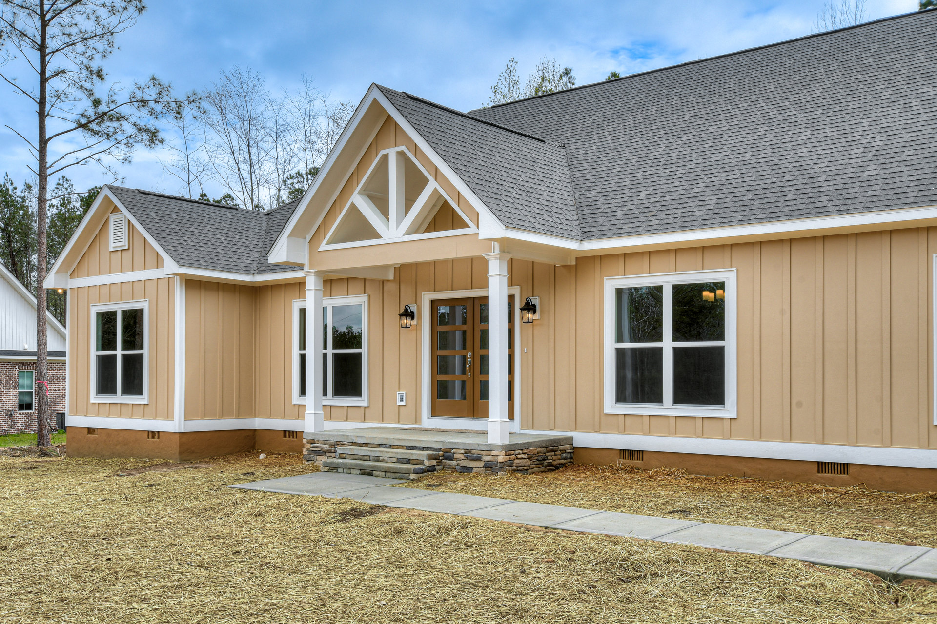 Brown-roofed house with white-framed windows, stone steps leading to a covered porch, driveway, and straw scattered on the ground
