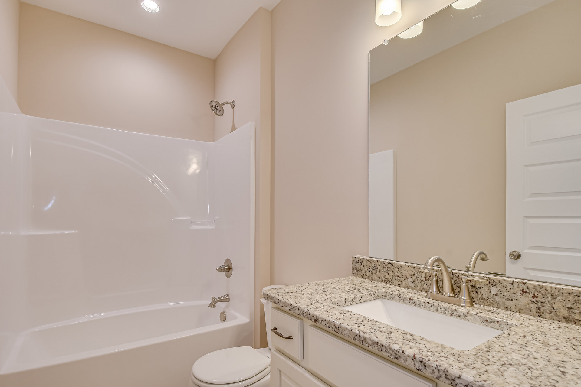Modern bathroom with white porcelain sink and chrome faucet, adjacent toilet with closed lid, glass-enclosed shower featuring wall-mounted showerhead, light gray tile walls, and
