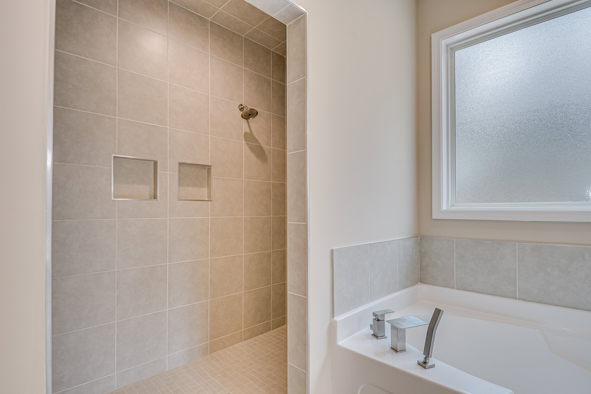 Bathroom featuring a freestanding bathtub with chrome faucet, glass-enclosed shower with wall-mounted shower head, white tile walls, built-in tile shelf, and frosted glass window
