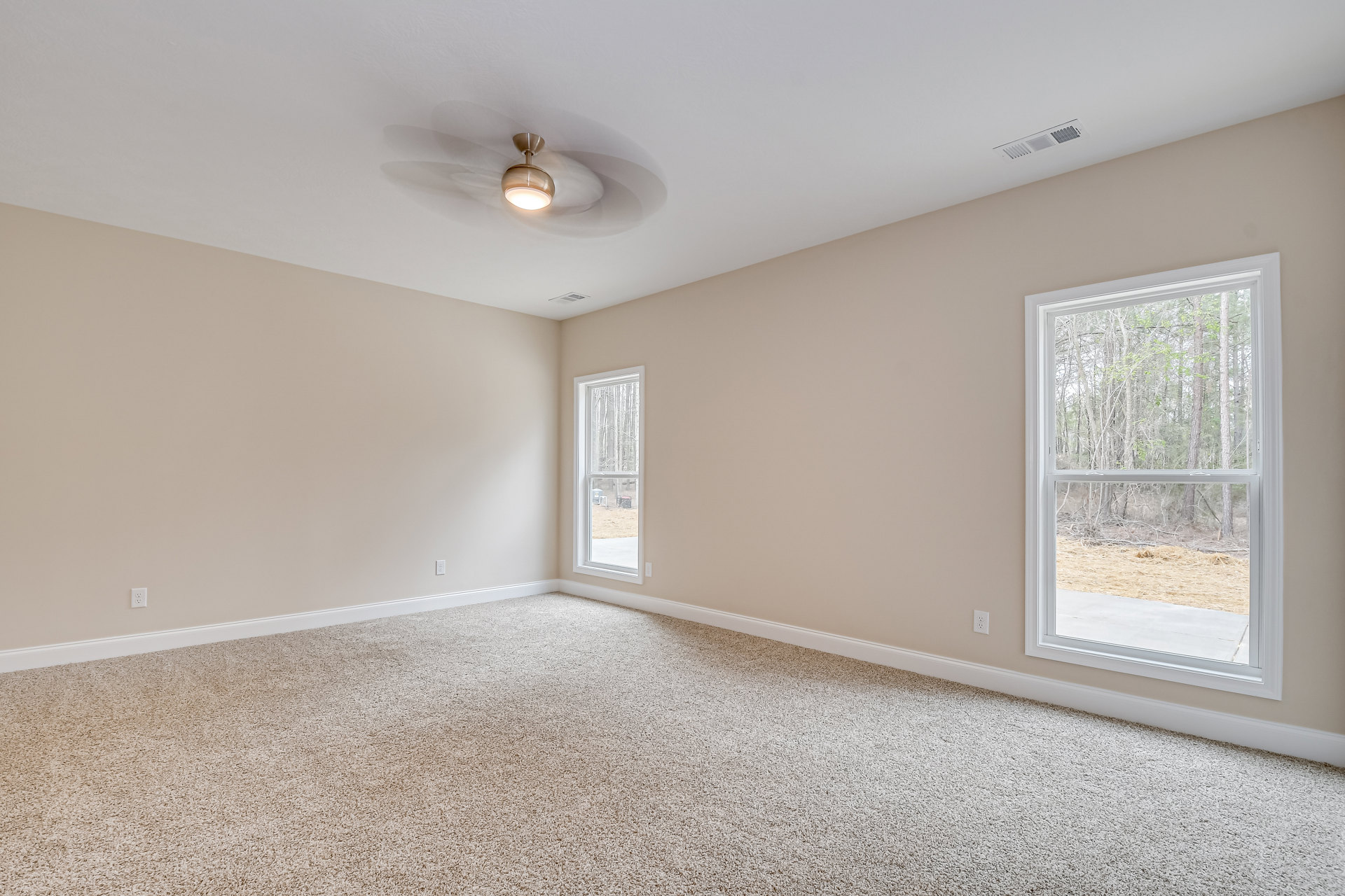 Carpeted room with white walls, large window overlooking trees, ceiling fan with light fixture, and ceiling vent