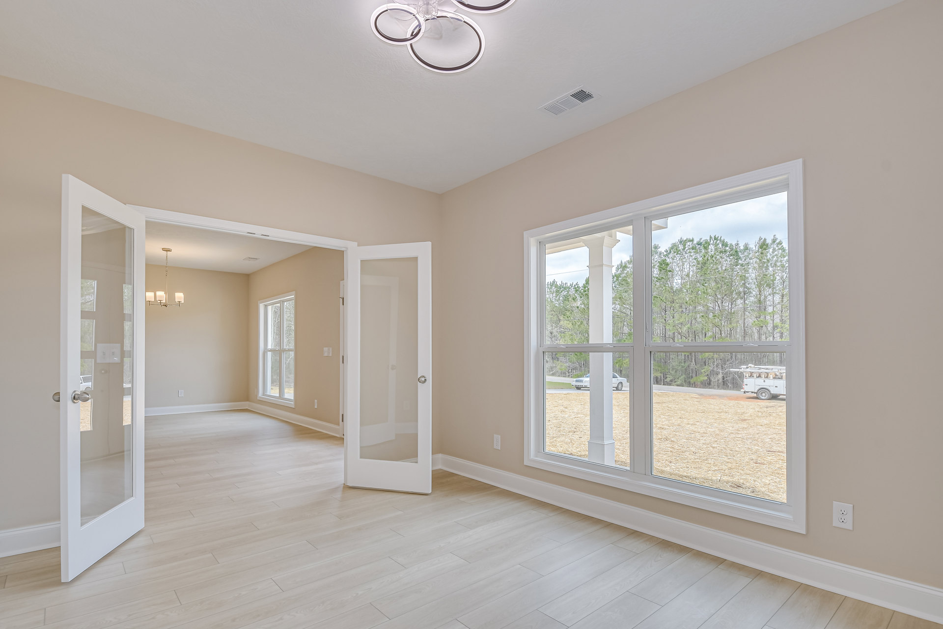 Spacious room featuring a large window with a white frame, wood flooring, white walls with plaster and molding, two doors including one with a silver knob, and a ceiling fan.
