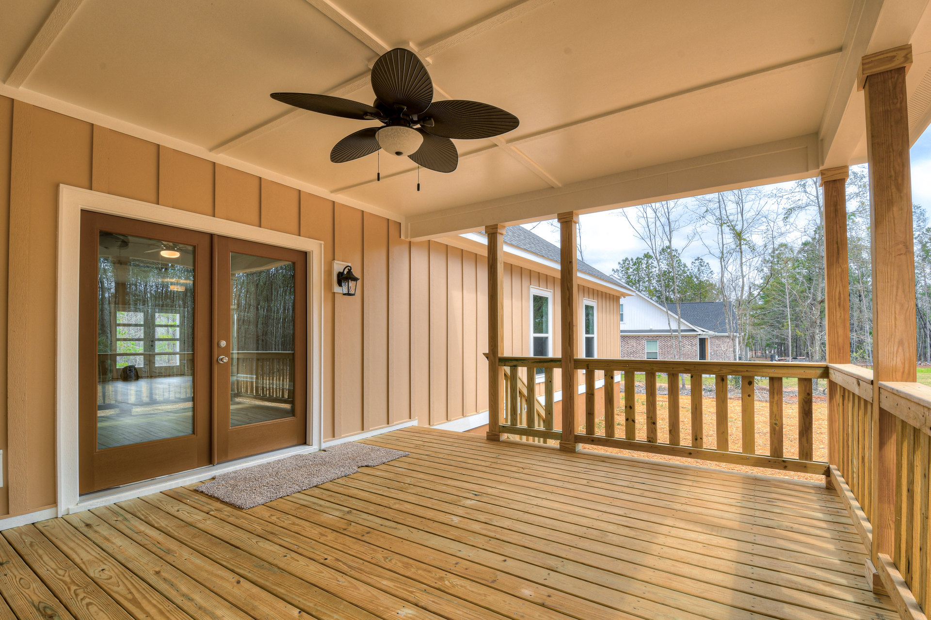 Wood deck with area rug, ceiling fan and light fixture overhead, double glass doors leading inside, white walls and windows surrounding porch.