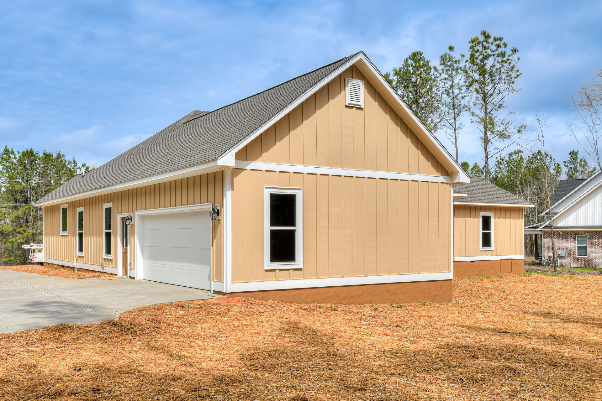 Two-story house with white siding, black-framed windows, attached white garage door, exterior wall vent, outdoor light fixture, and a small pile of hay on the driveway, set against