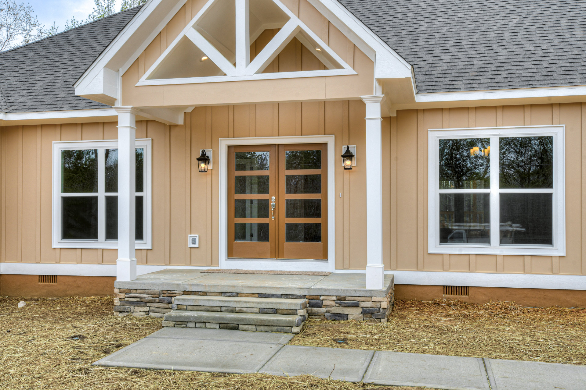 Stone steps leading to a covered porch with white wood beams, double glass-panel doors, and large windows reflecting trees