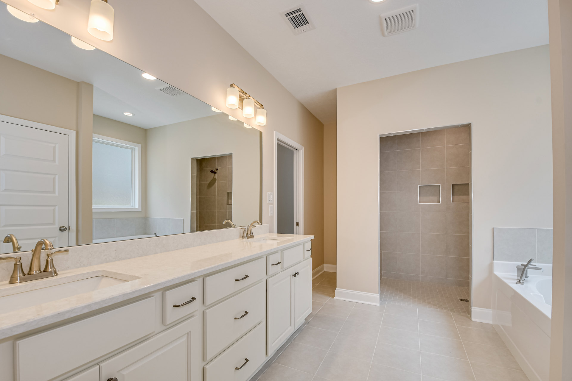 Bathroom featuring a wide mirror above a white vanity, spacious glass-enclosed shower with tile walls and built-in square shelf, chrome faucet, window, and paneled white door