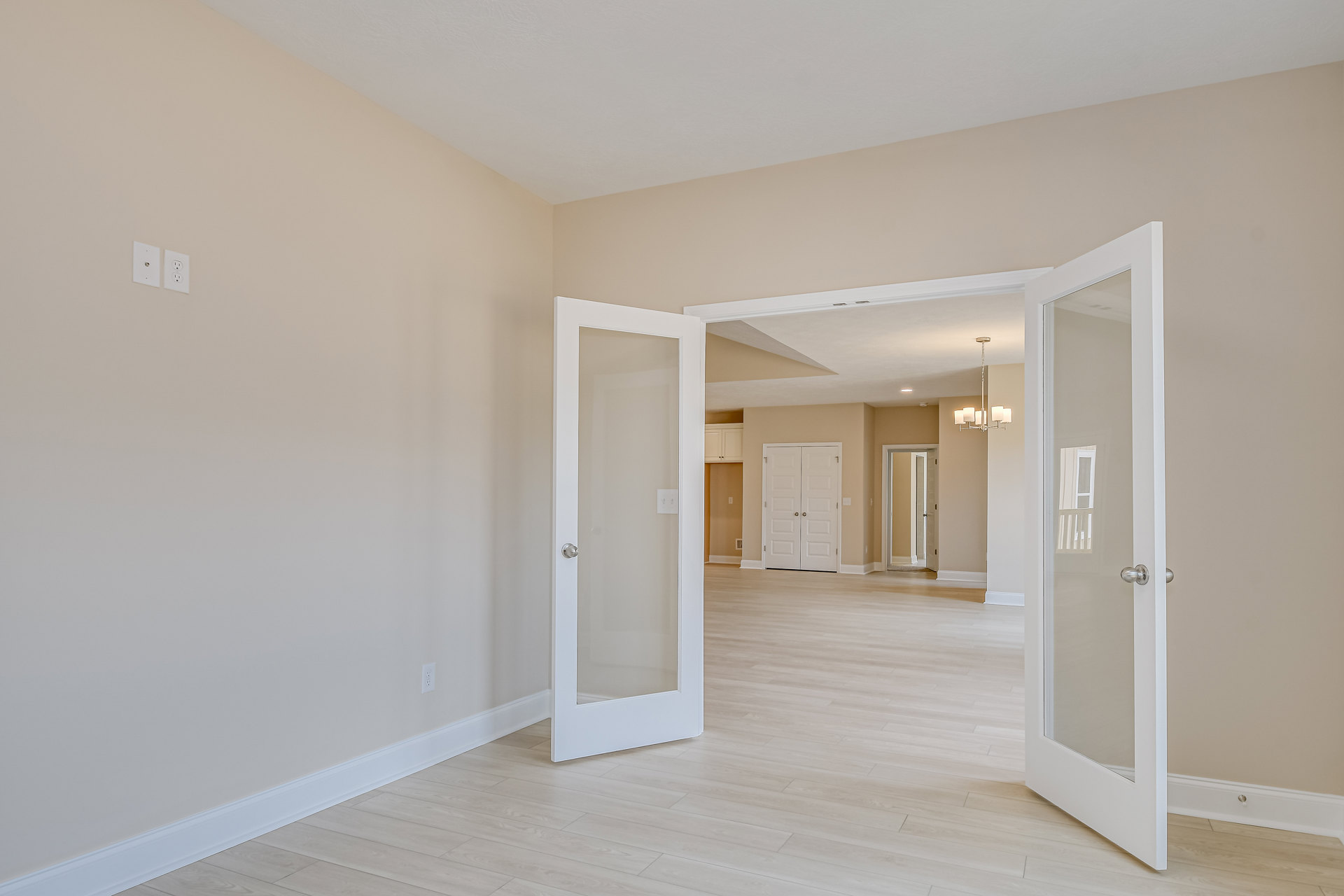 Hardwood floor room with white double doors featuring silver handles, glass door with silver knob, white walls, ceiling molding
