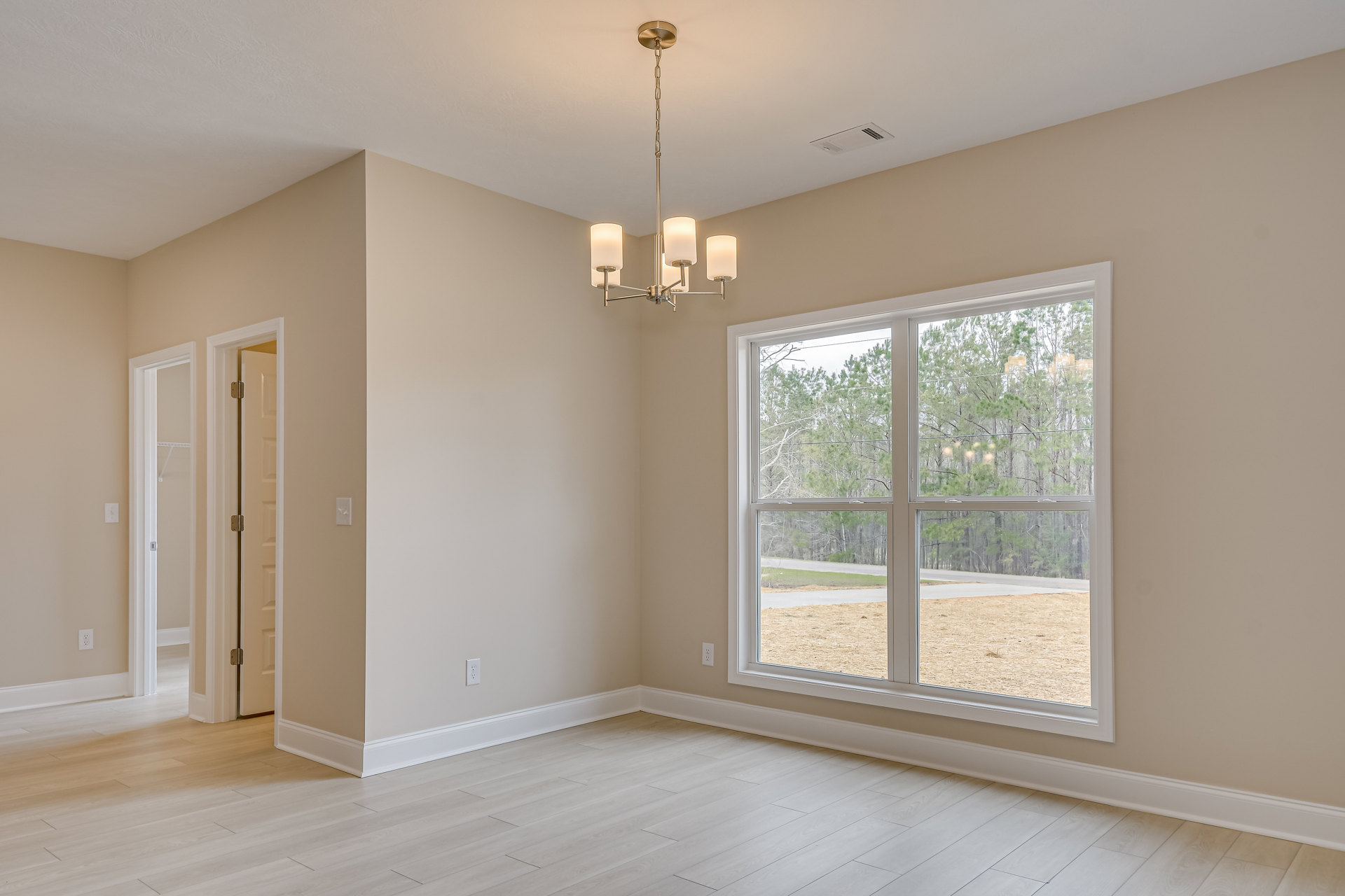 White wood floor and white walls, large window with trees visible outside, ceiling-mounted chandelier, door with metal hinge, decorative molding along walls and ceiling.