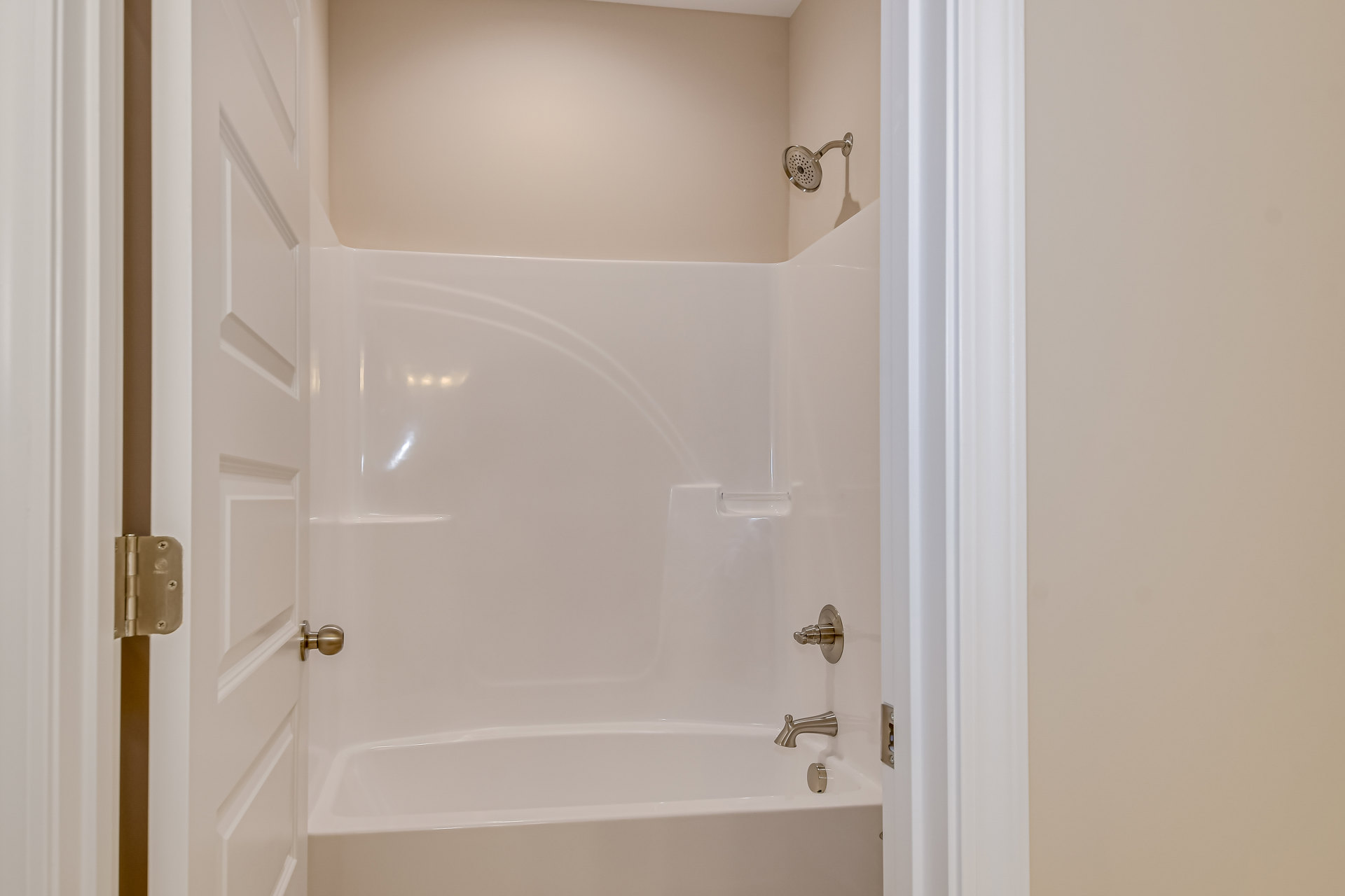 Freestanding white bathtub with chrome faucet against light plaster wall, adjacent to modern shower head and brushed metal door hinge