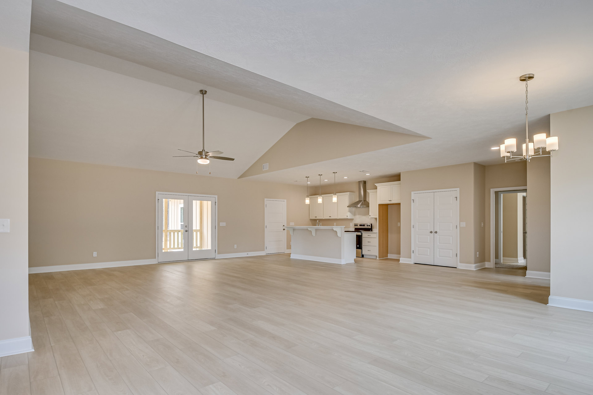 Spacious open-plan room with wood flooring, ceiling fan, glass-paneled double doors, white double door with silver handles, and adjacent kitchen and dining area