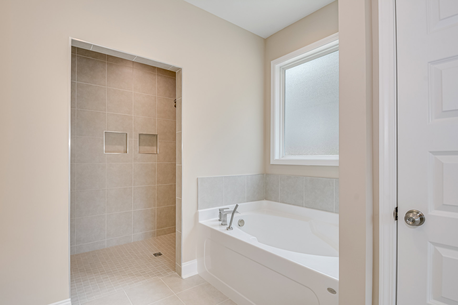 White tile bathroom featuring a built-in bathtub with silver faucet, glass-enclosed shower, two recessed square shelves, and a window above the tub.