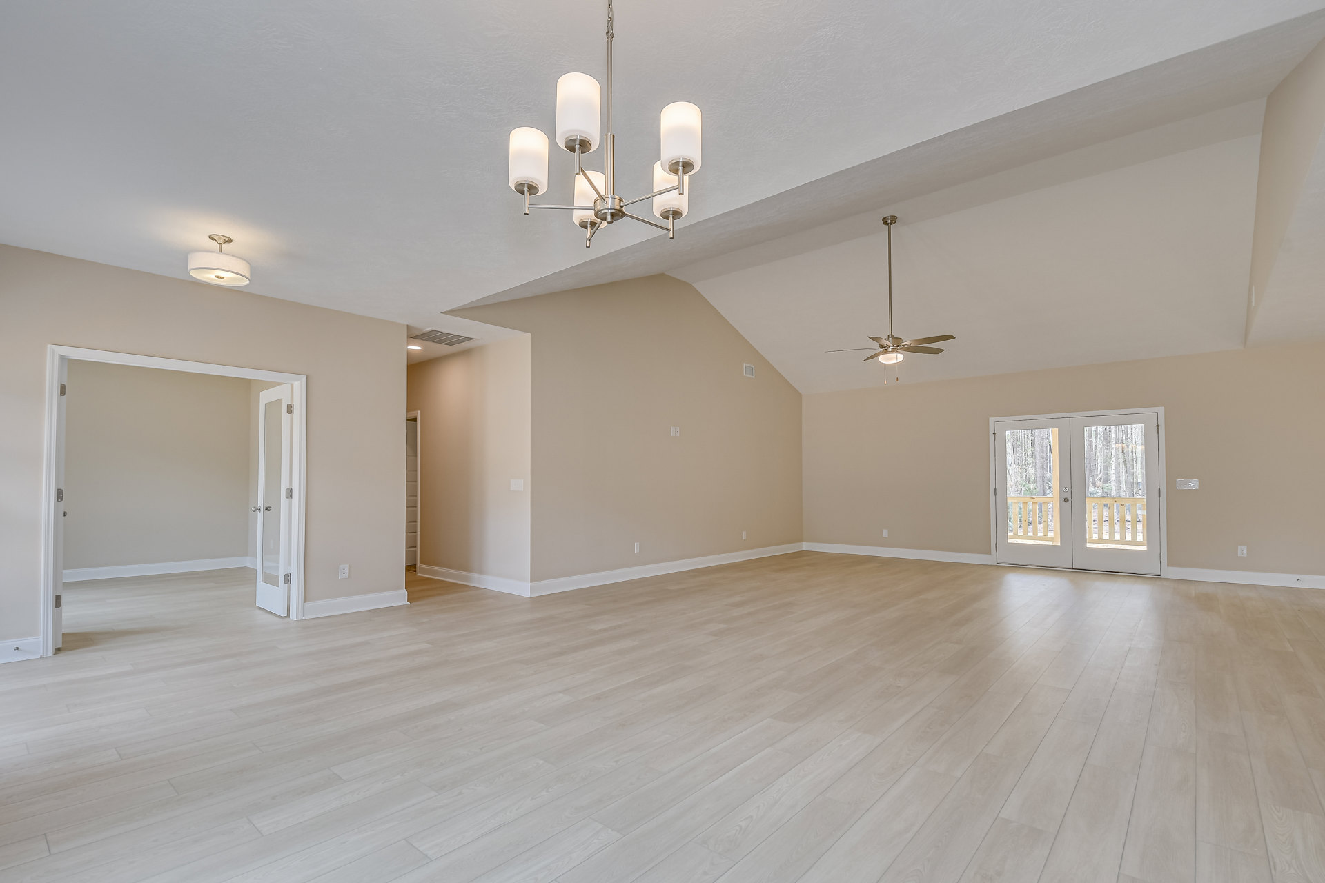 Spacious room with hardwood flooring, ceiling fan with light, double glass-paneled doors, white-shaded light fixture, white walls with crown molding