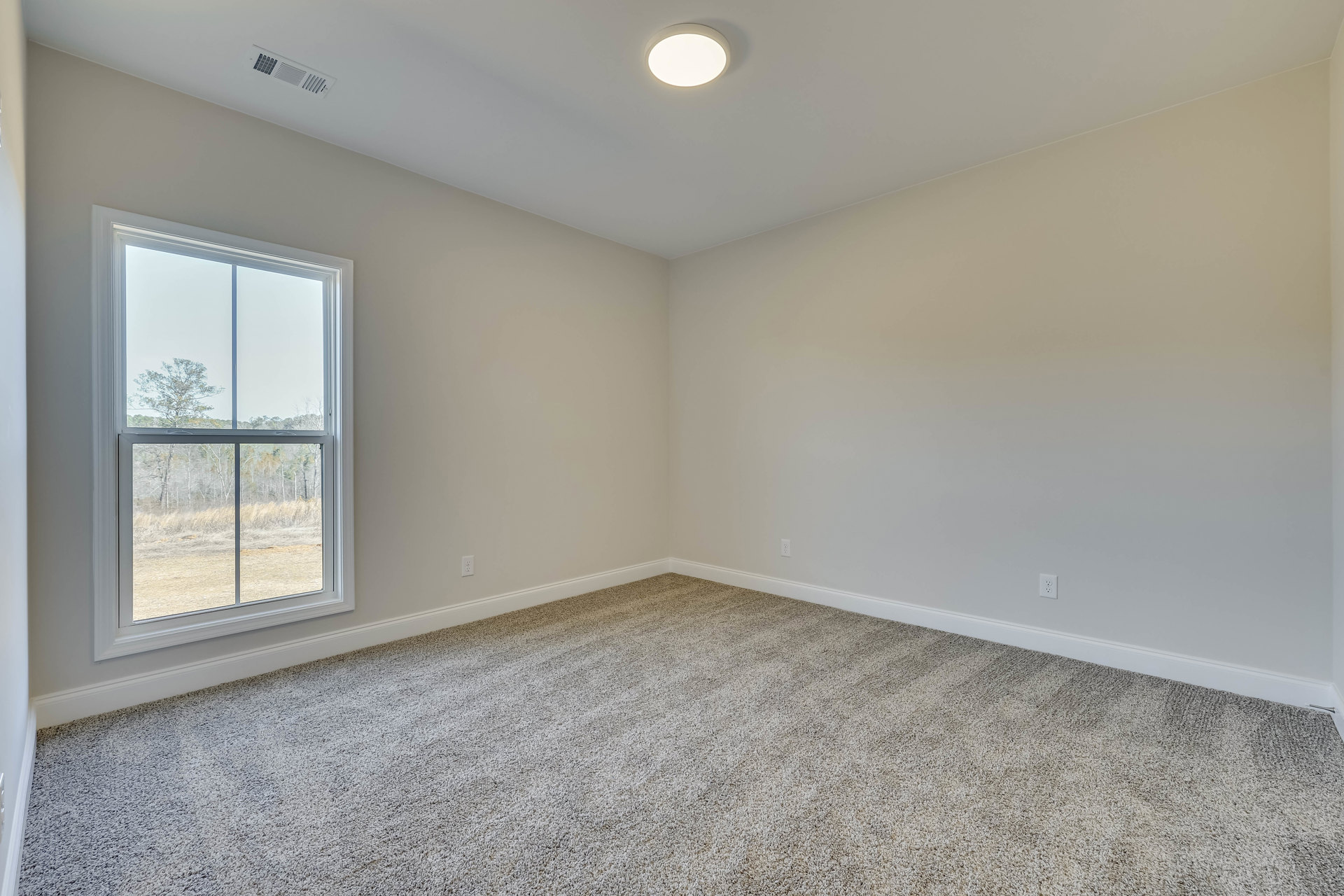 Carpeted room with white walls, ceiling vent, recessed light, large window overlooking leafy trees