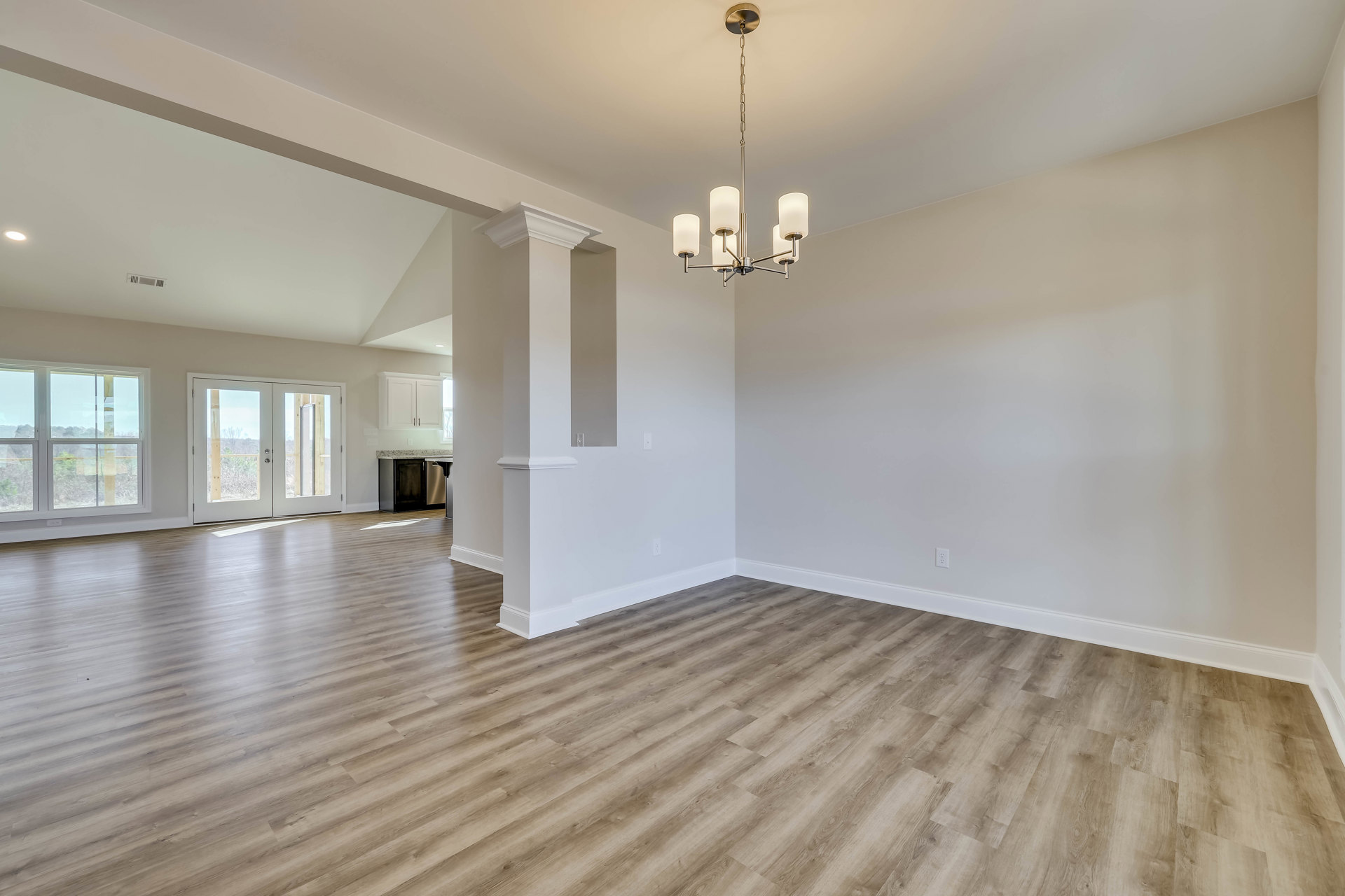 Wood flooring, white walls, glass-paneled double doors, window with outdoor view, chandelier, and countertop in a spacious room