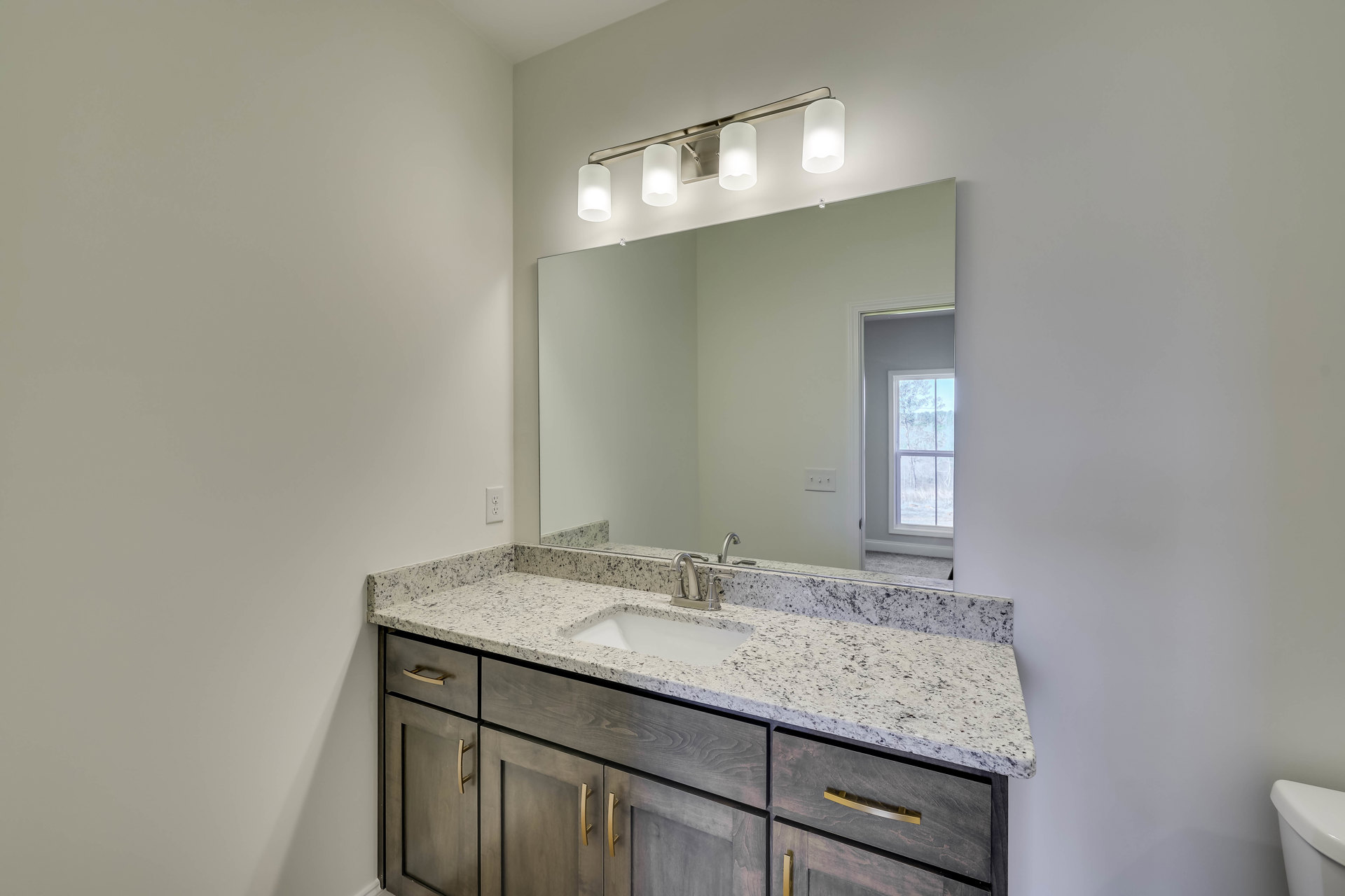 Bathroom with white tile walls, wood cabinetry, stone countertop, rectangular mirror above sink, and modern light fixture with frosted glass shades.