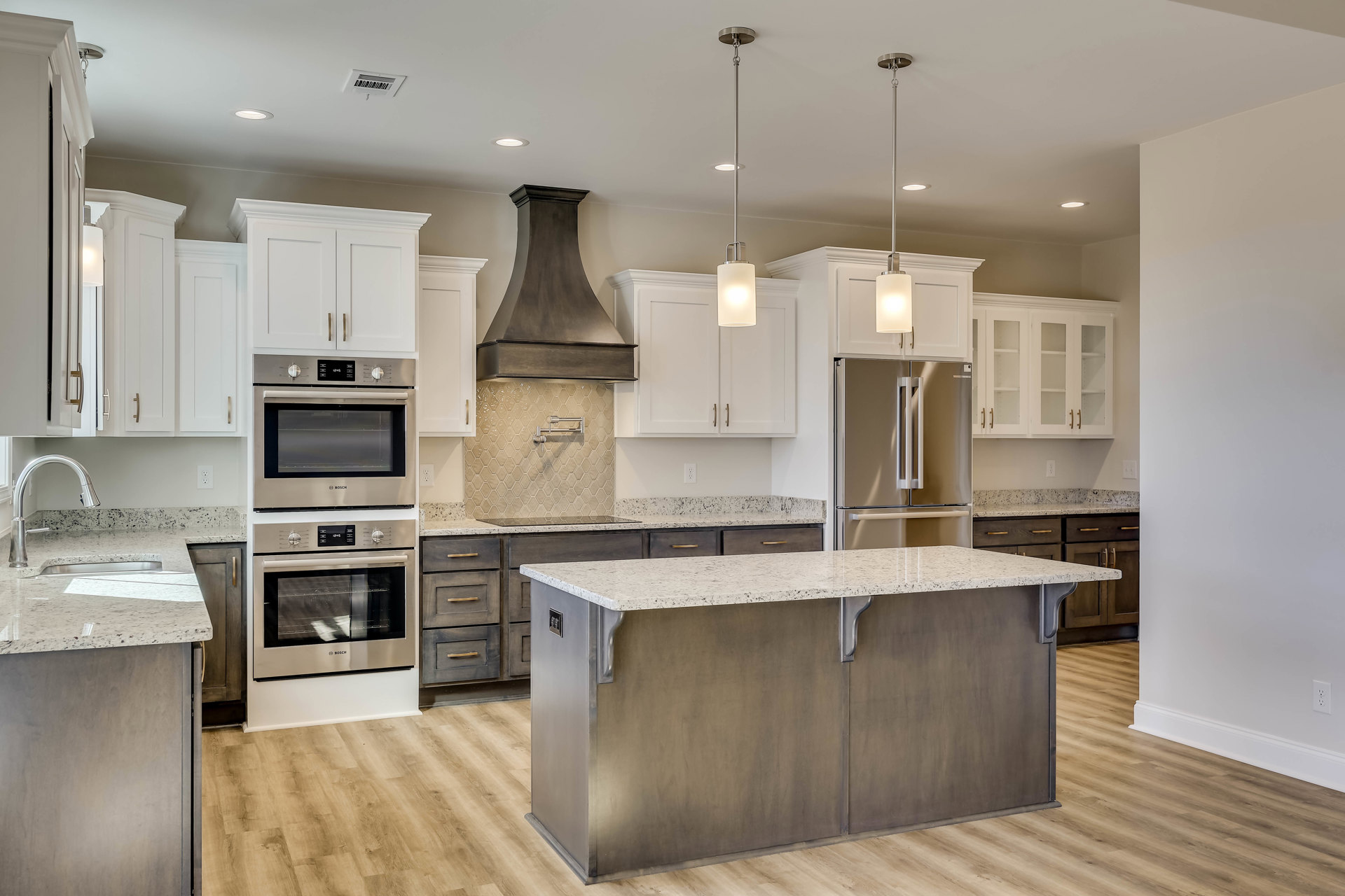 Spacious kitchen featuring a large central island with white cabinetry, glass-front upper cabinets, stainless steel oven with visible knobs and dials, and stone countertops.